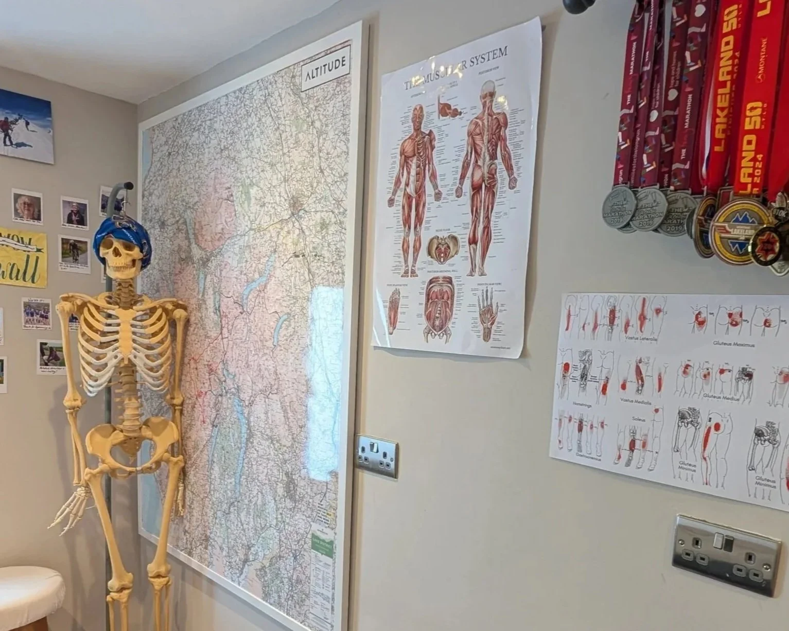 A room with a skeleton model, a large detailed map of the lake district on the wall, and posters of the muscular system and muscles on the wall. There are medals hanging on the wall.