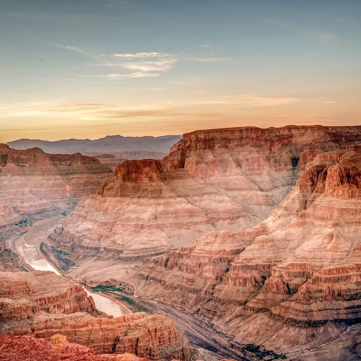 Sunset over the Grand Canyon with layered red rock formations and the Colorado River at the bottom.