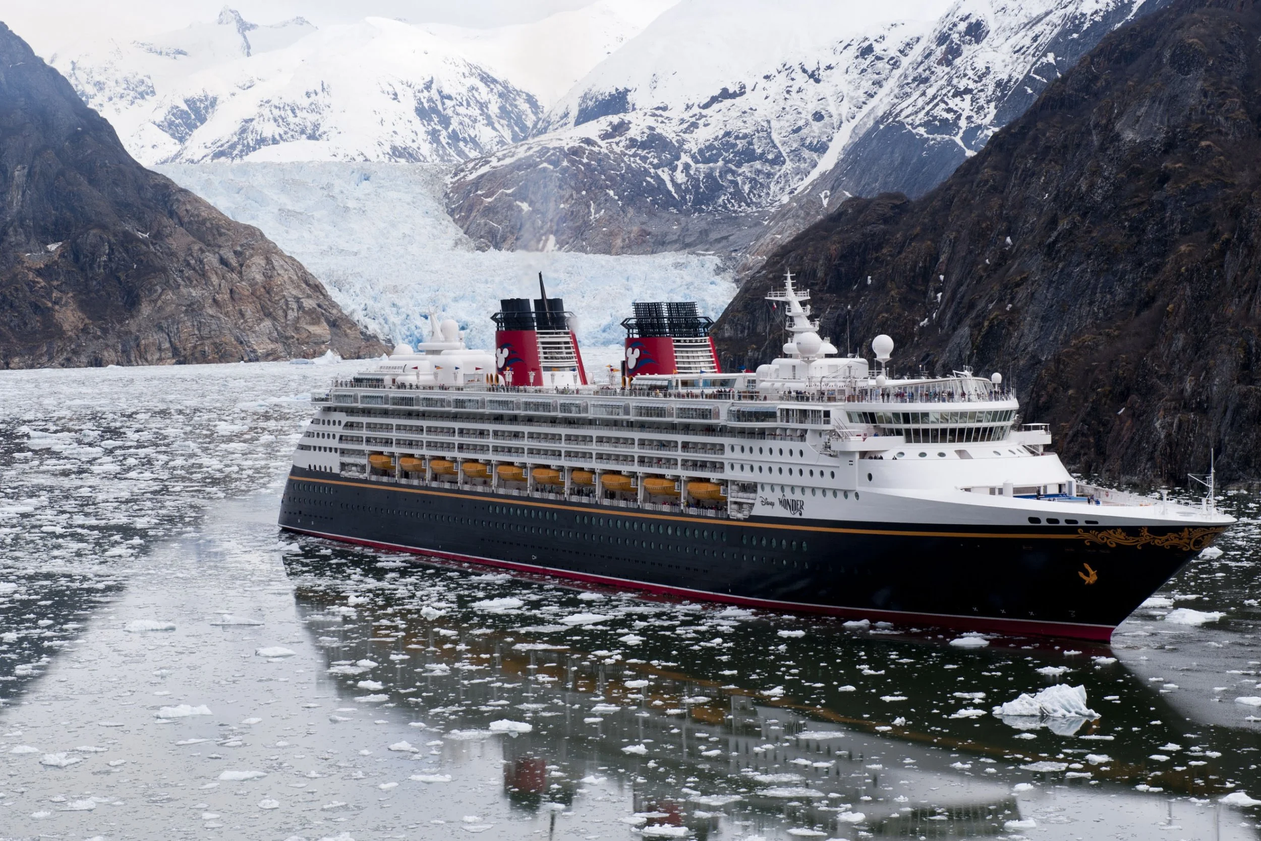 A large cruise ship sailing through icy waters surrounded by snow-covered mountains.