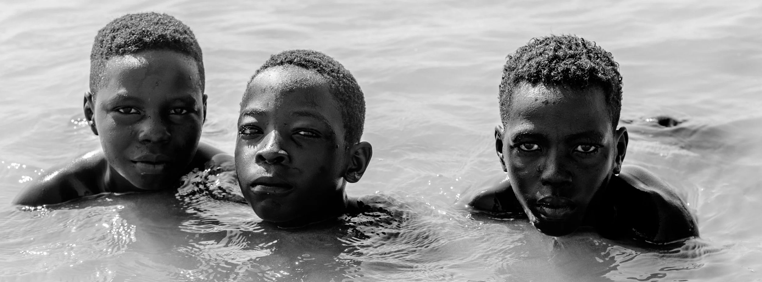 Three boys swimming in water, looking directly at the camera.