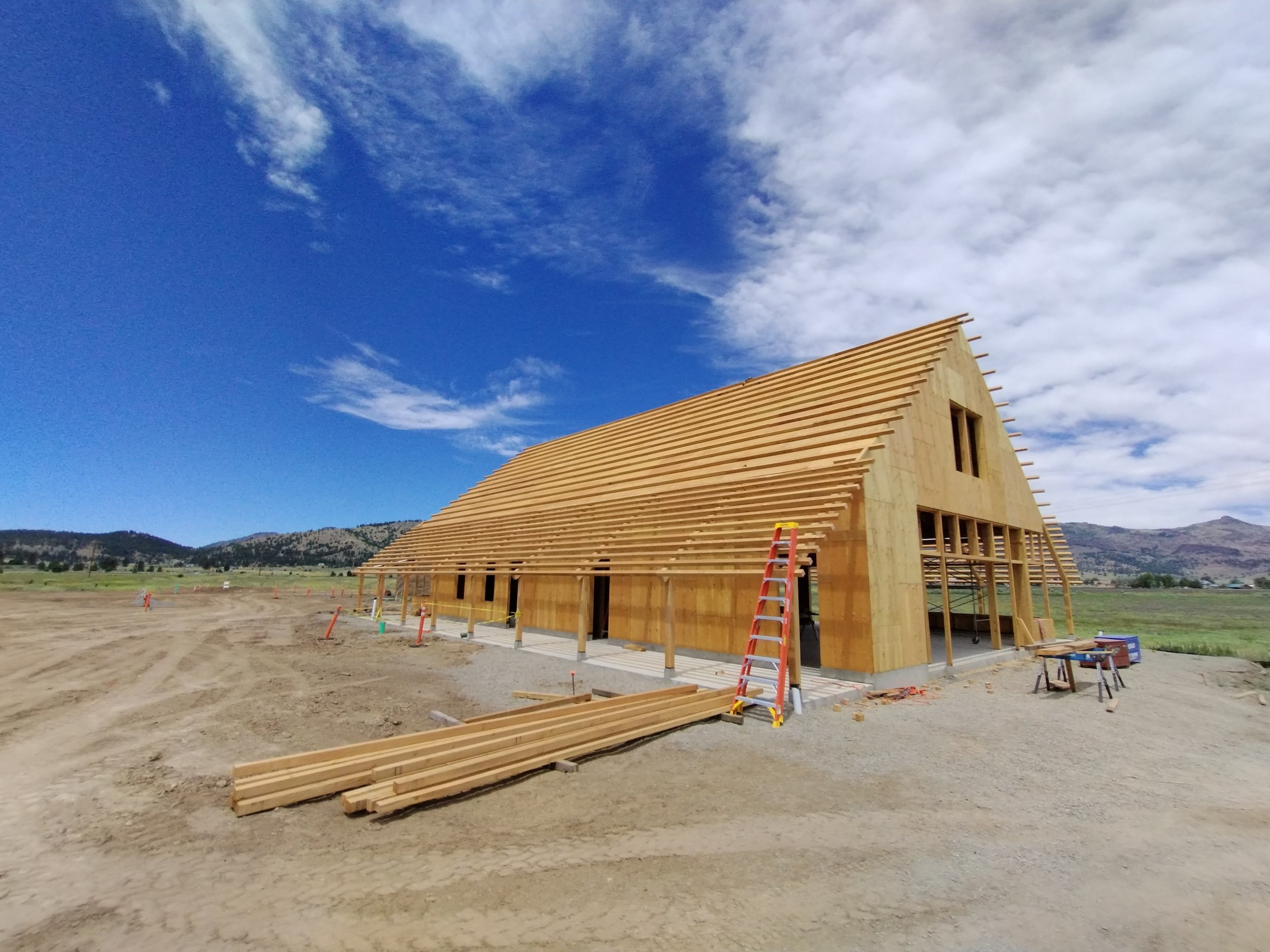 Construction site with a wooden building under construction and a bright blue sky with clouds.