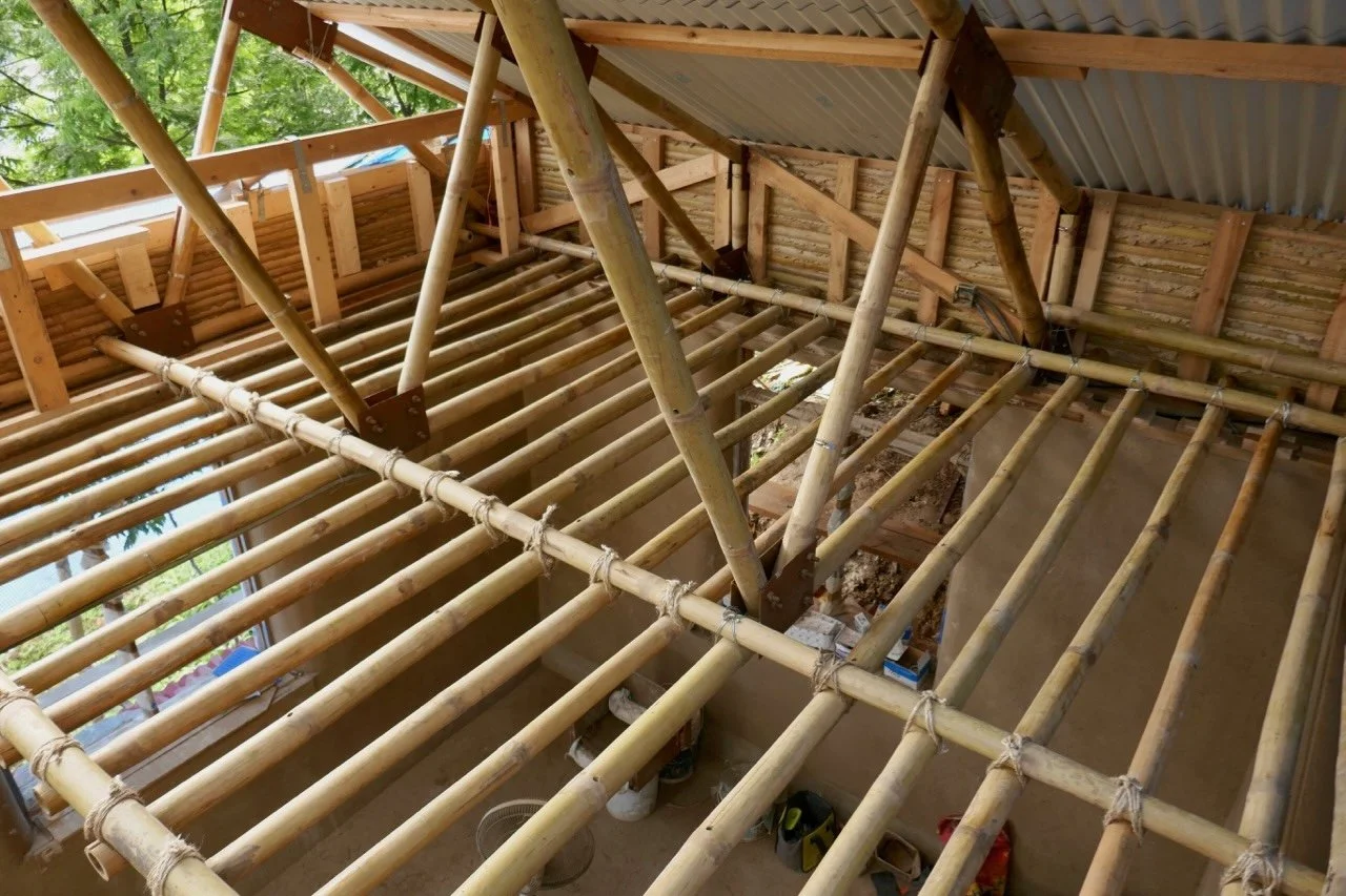 Interior view of a building under construction with bamboo and wooden framing, and metal roofing panels installed.