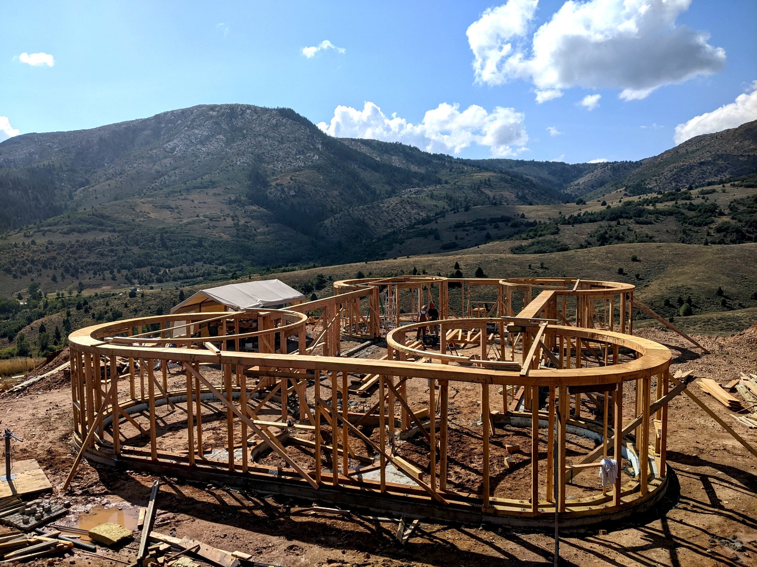 House under construction on a hillside with mountains and a partly cloudy sky in the background.