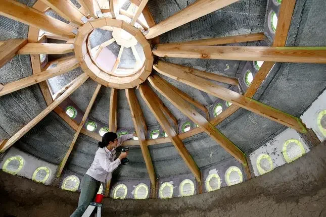 Interior view of a circular construction with a wooden framework and a woman working inside.