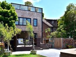 Modern multi-story house with a backyard featuring patio furniture, trees, and a wooden fence.