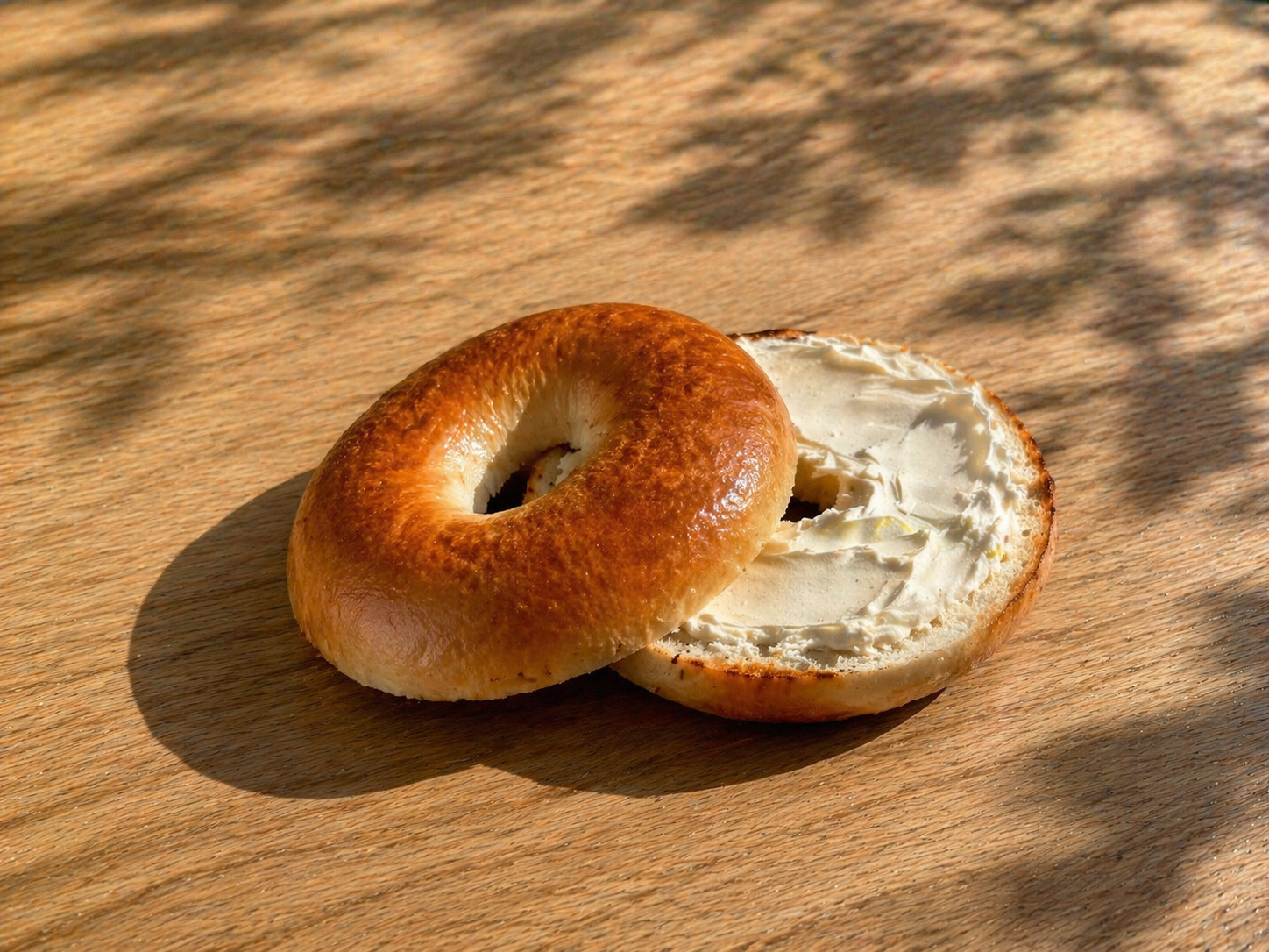 Bagel with cream cheese on a wooden surface with shadows.