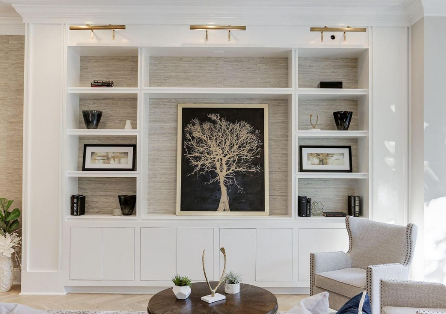 Living room with white built-in wall shelves, a large framed art of a tree, gray armchair, and a round coffee table with decorative items.