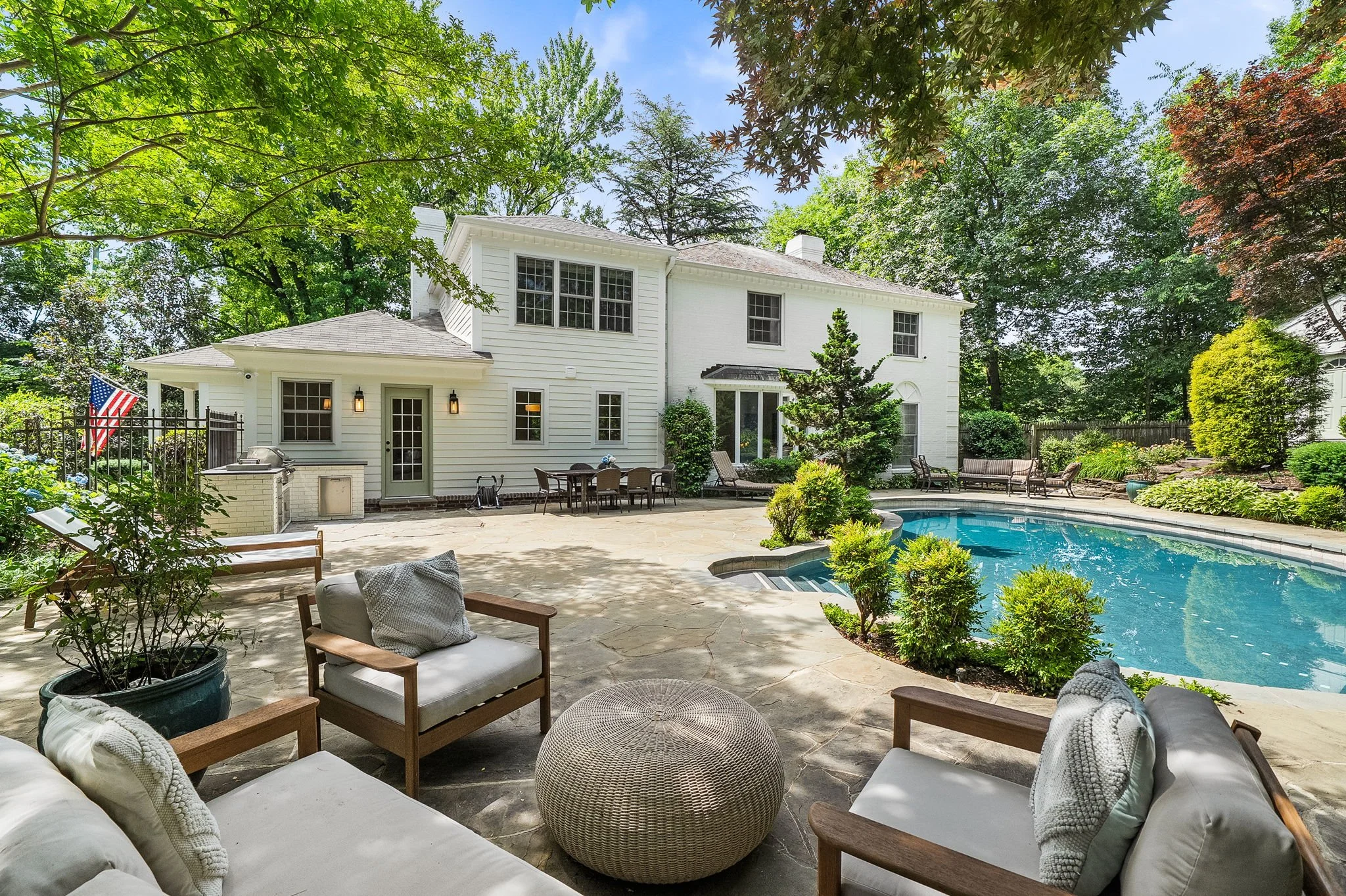 Backyard of a house with a swimming pool, outdoor furniture, and surrounded by trees.
