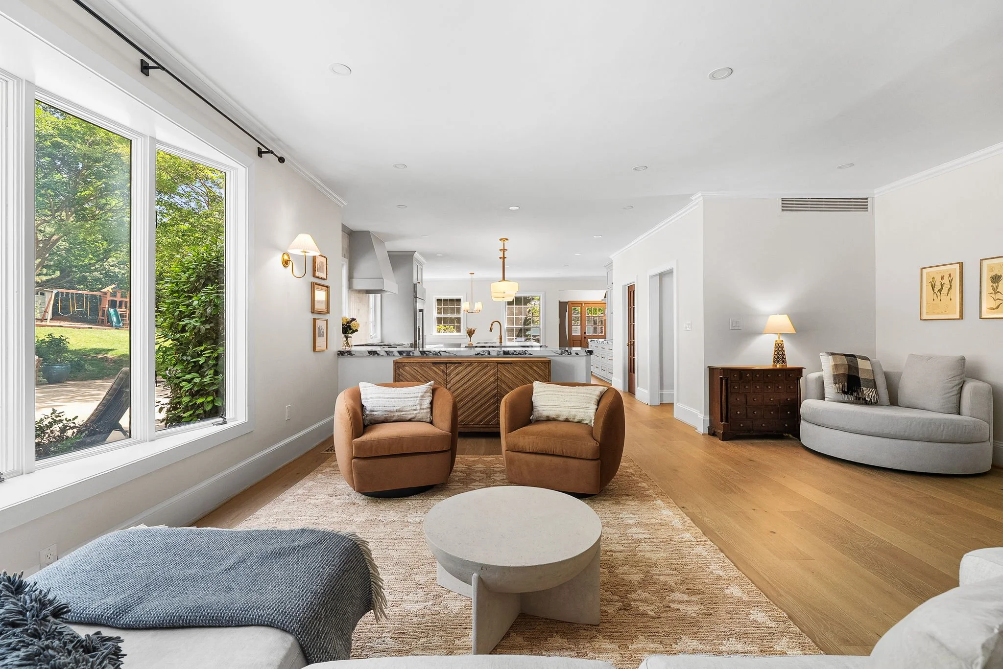 Living room with large windows, wood flooring, beige and white furniture, and artwork on the walls.