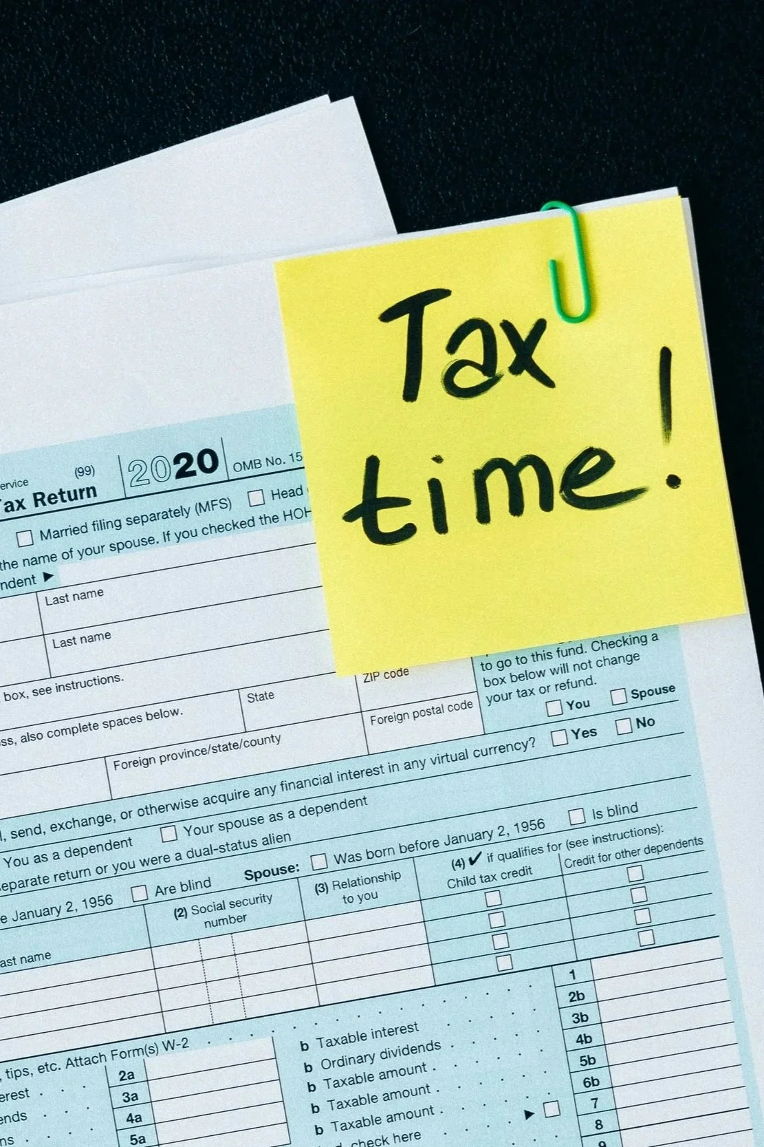 A tax form with a yellow sticky note that says 'Tax time!' attached with a green paperclip.