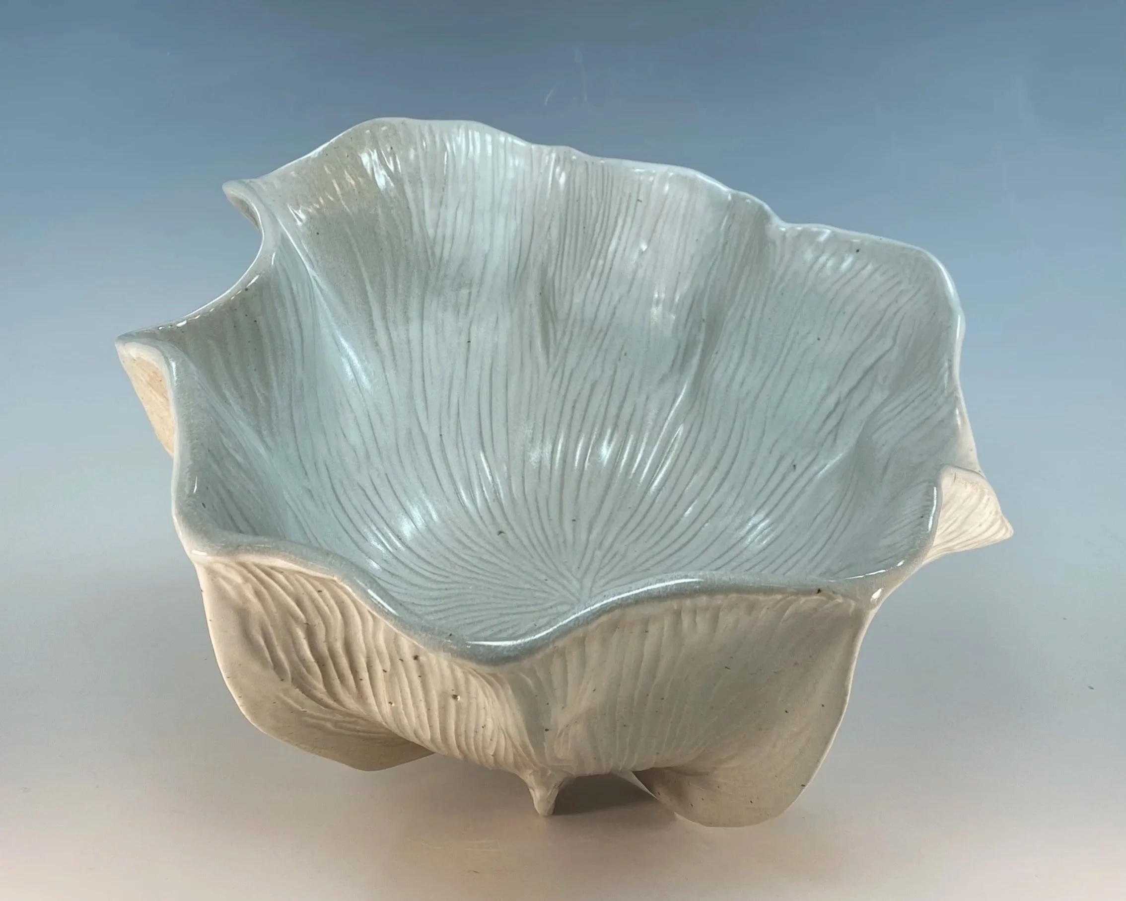 Close-up of a white ceramic seashell-shaped dish with textured ridges and a glossy finish, on a plain light background.