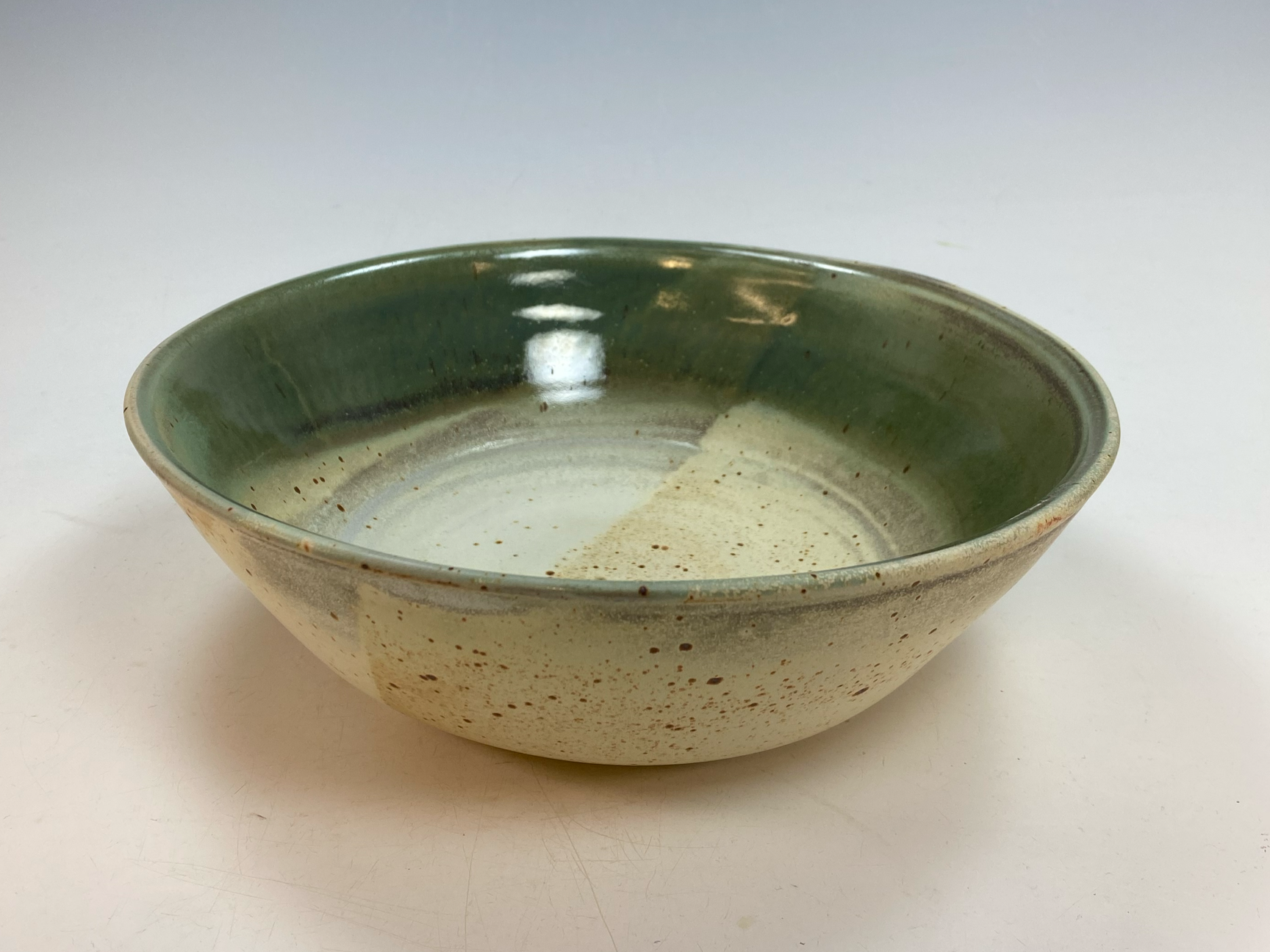 A ceramic bowl with a green glaze on the inside and a speckled beige exterior, sitting on a white surface.