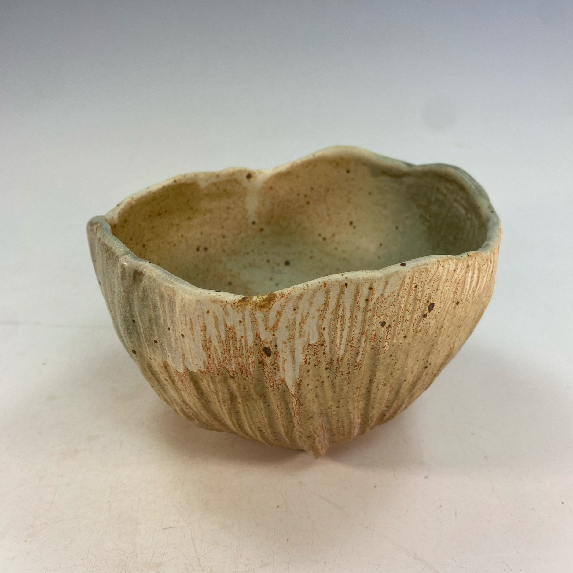 Close-up of a handmade ceramic bowl with a textured, striped exterior and a smooth, speckled interior, placed on a plain white surface.