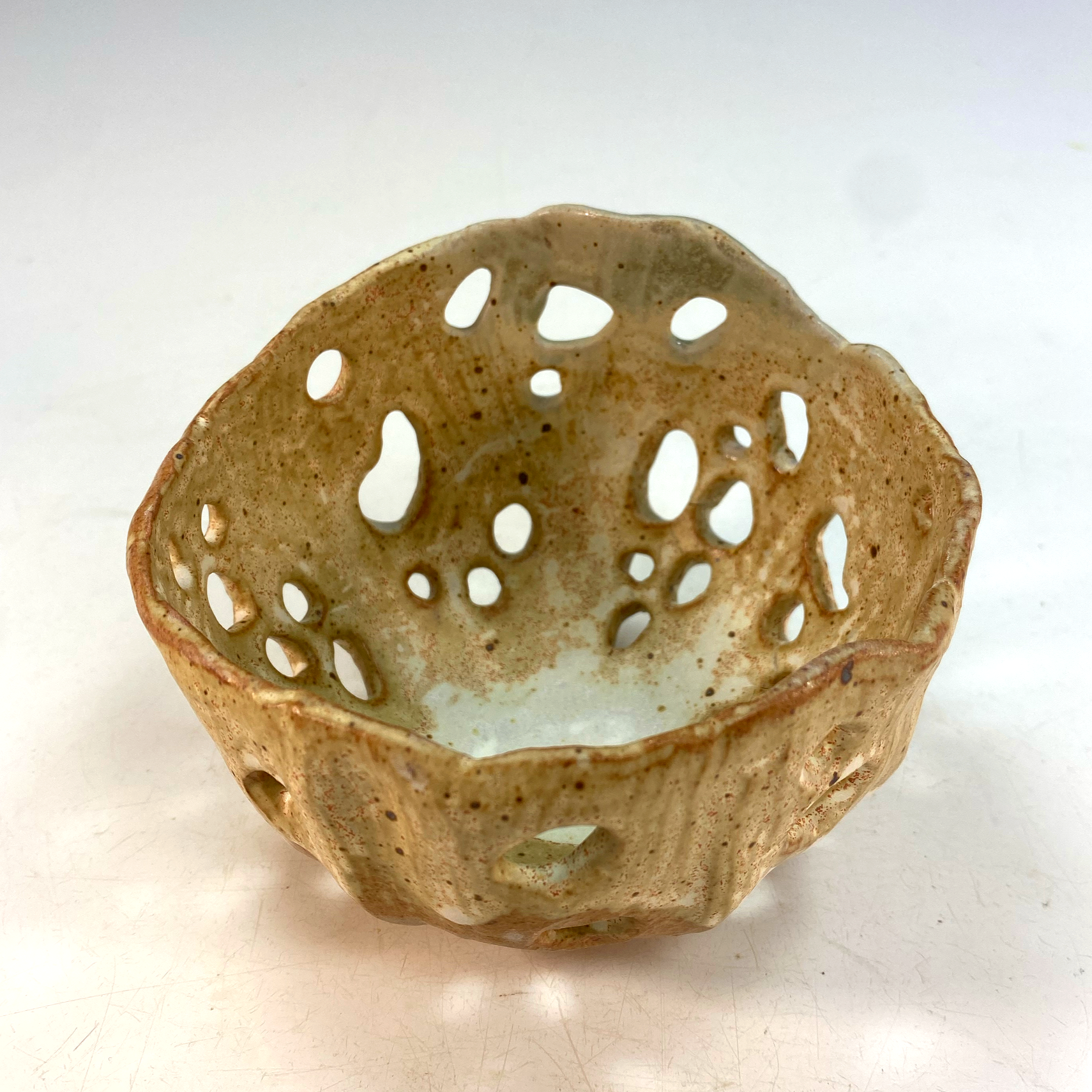 A decorated ceramic lantern with an intricate lattice pattern, placed on a white surface.