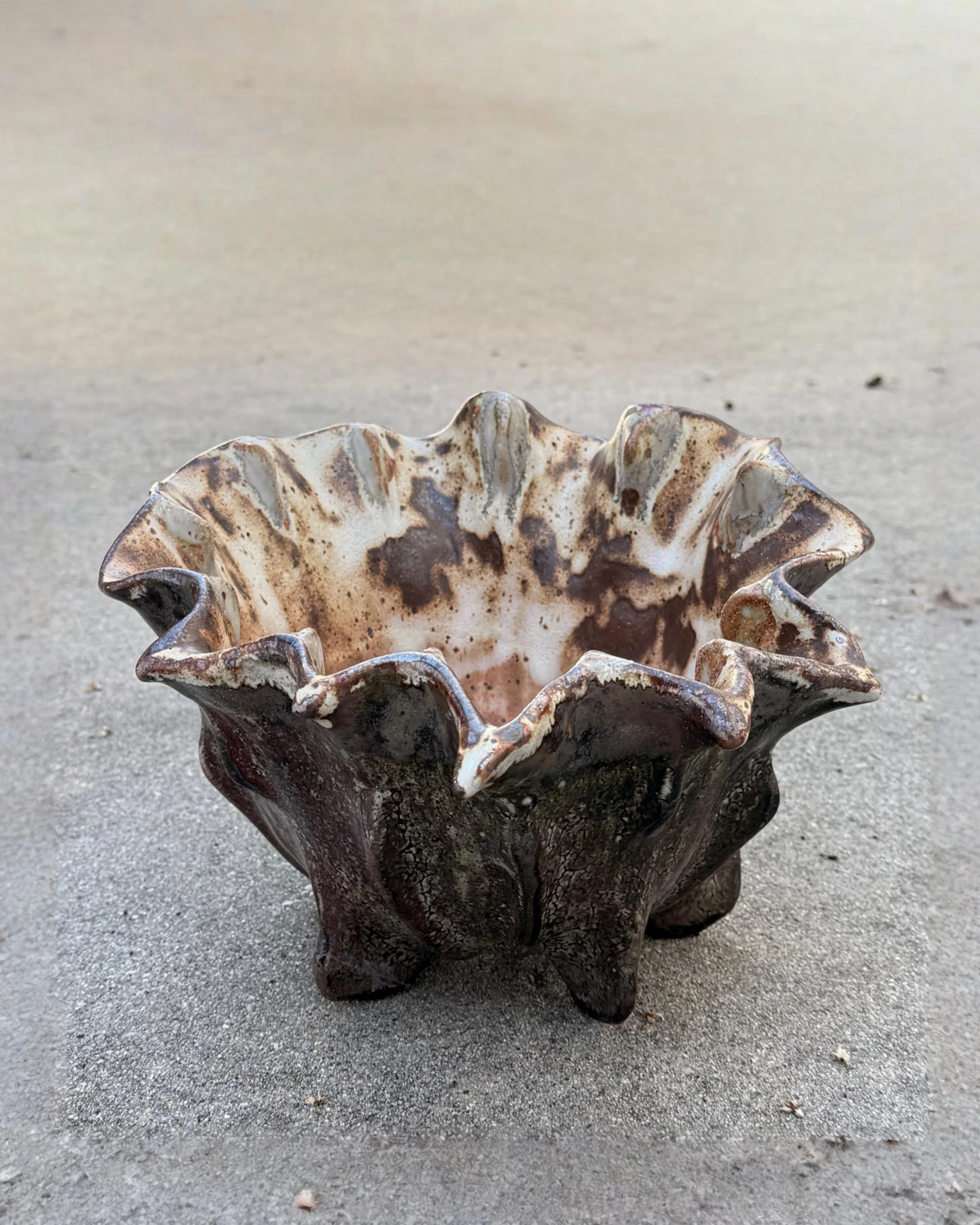 Decorative spiky prehistoric ceramic bowl with a deep rustic burgundy marbled pattern, placed on a gray concrete surface.