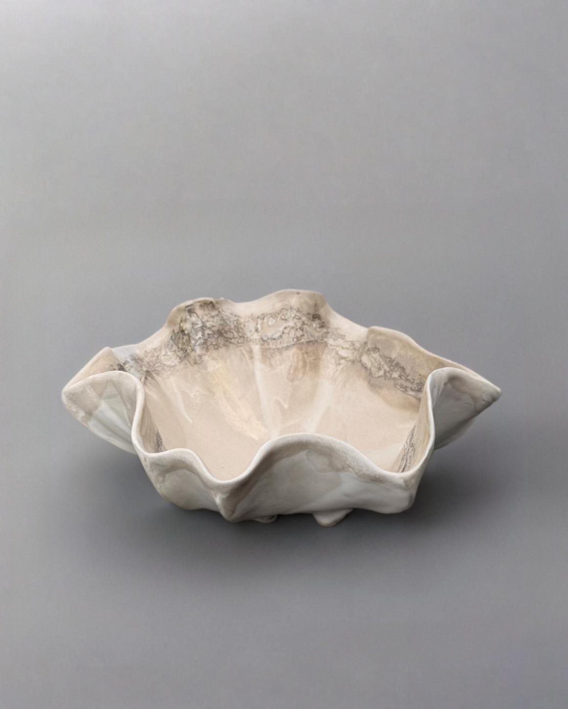 A ceramic bowl with a wavy, ruffled edge and a creamy, marbled pattern, placed on a plain grey background.