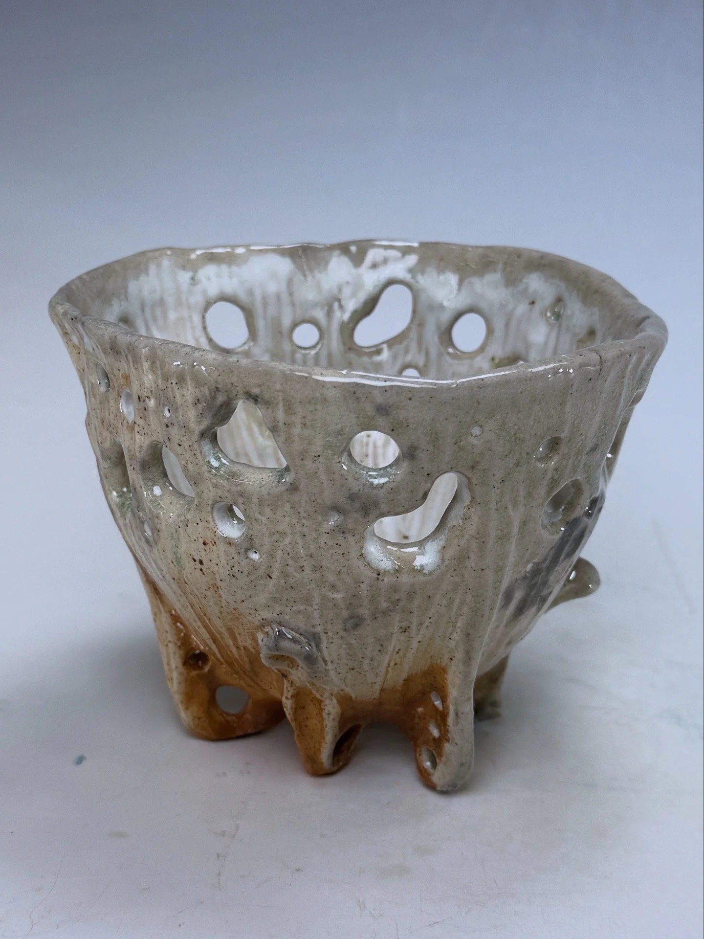 A ceramic vase with a textured, irregular surface and multiple circular holes, featuring a gradient of colors from gray to brown.