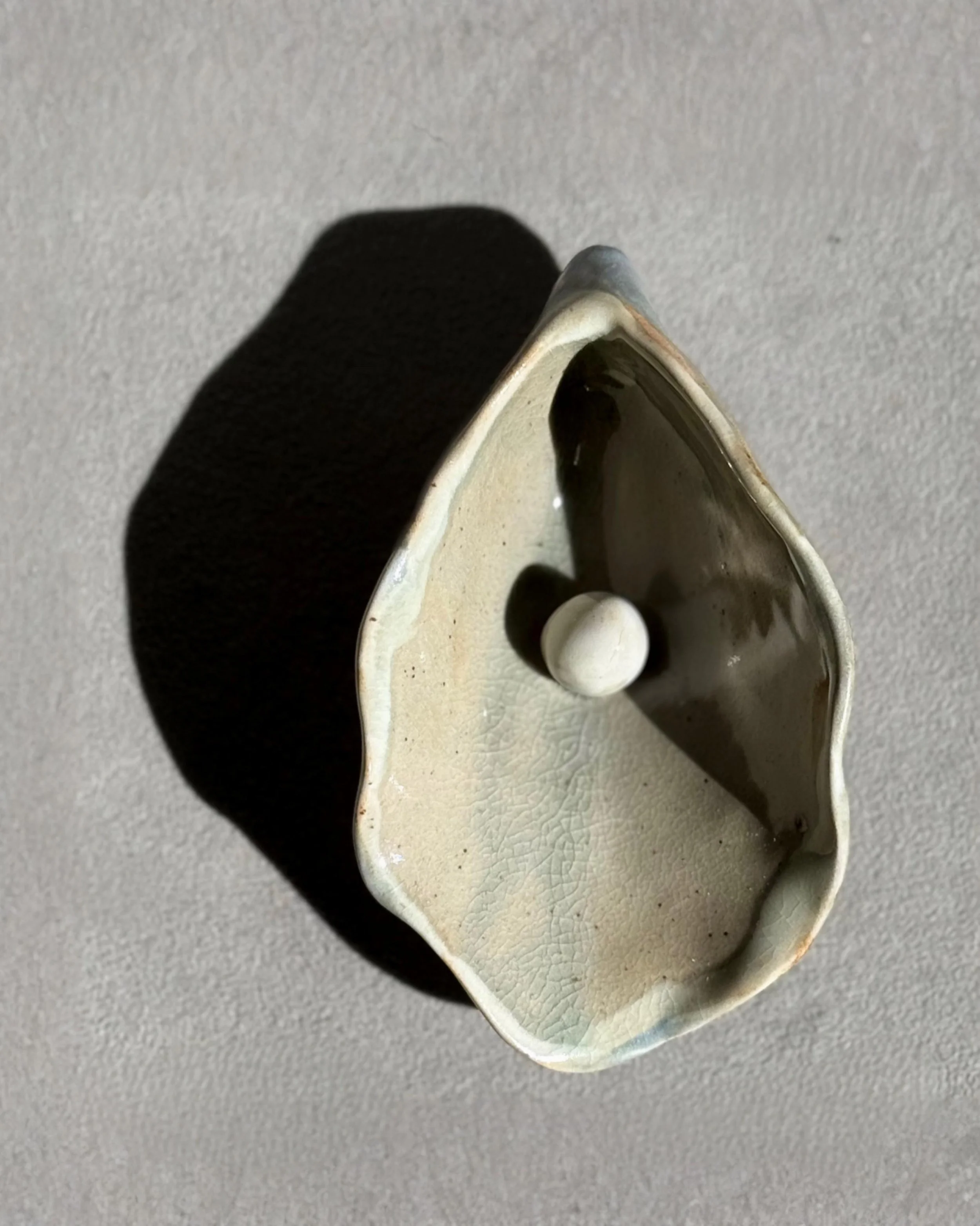 Ceramic dish with a white exterior and dark brown interior containing a small white spherical object, placed on a gray textured surface.