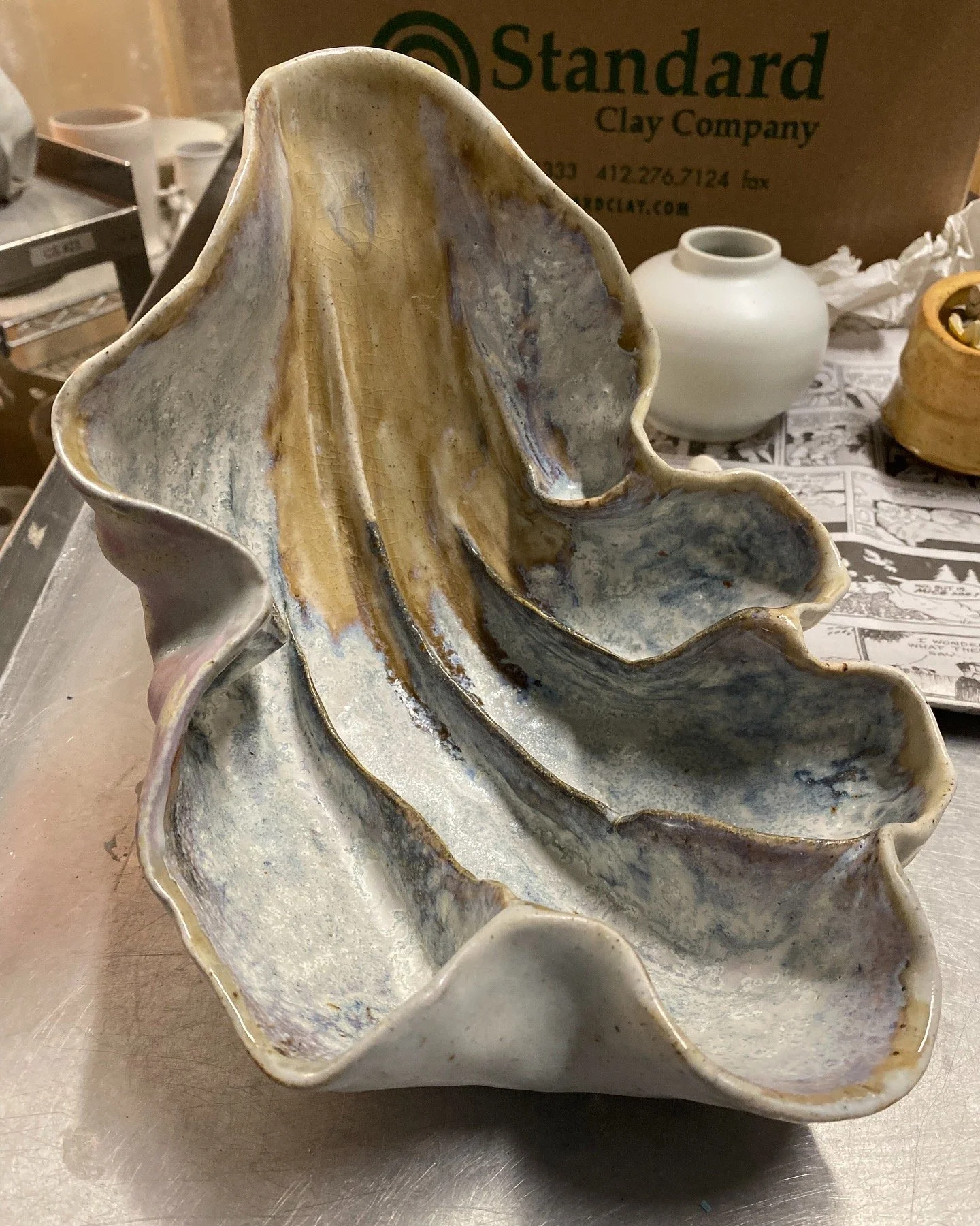 An irregularly shaped ceramic vessel with a ruffled edge, featuring a glazed surface with earthy tones and textured patterns.