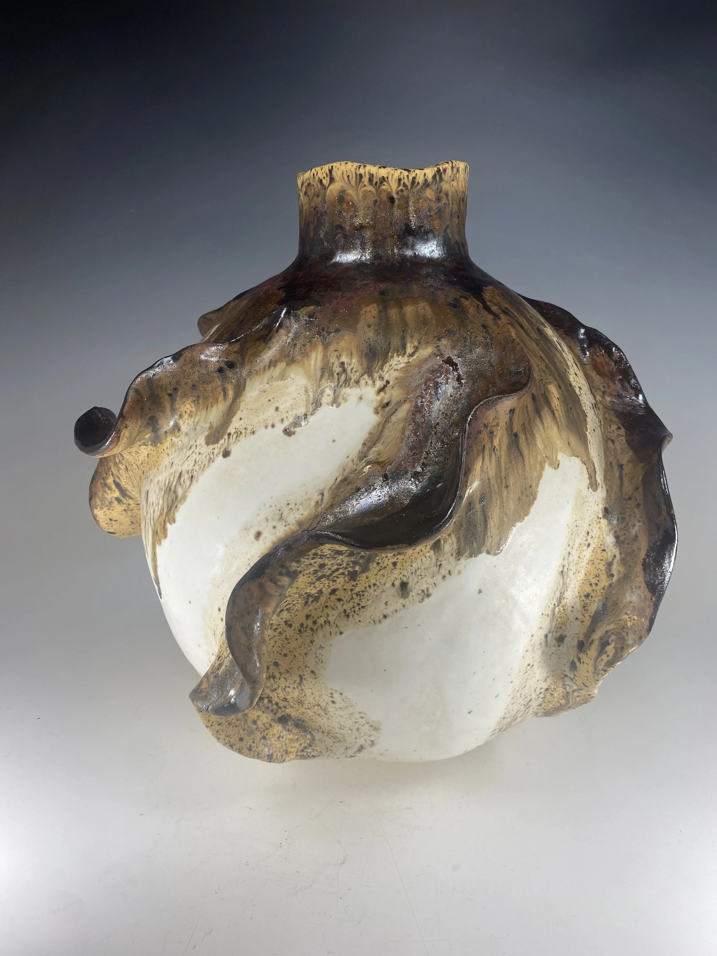 Ceramic vase lamp with wavy, textured surface and earth-tone glaze, set against a plain gray background.