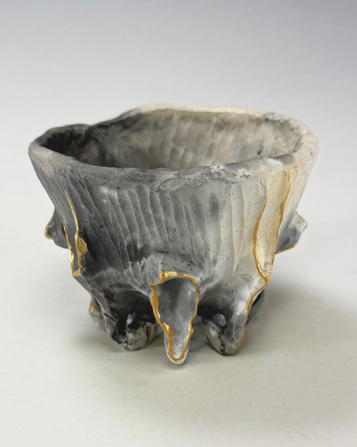 A decorative bowl made of agate with gold edges, showcasing gray, white, and black banded patterns, placed on a plain white surface.