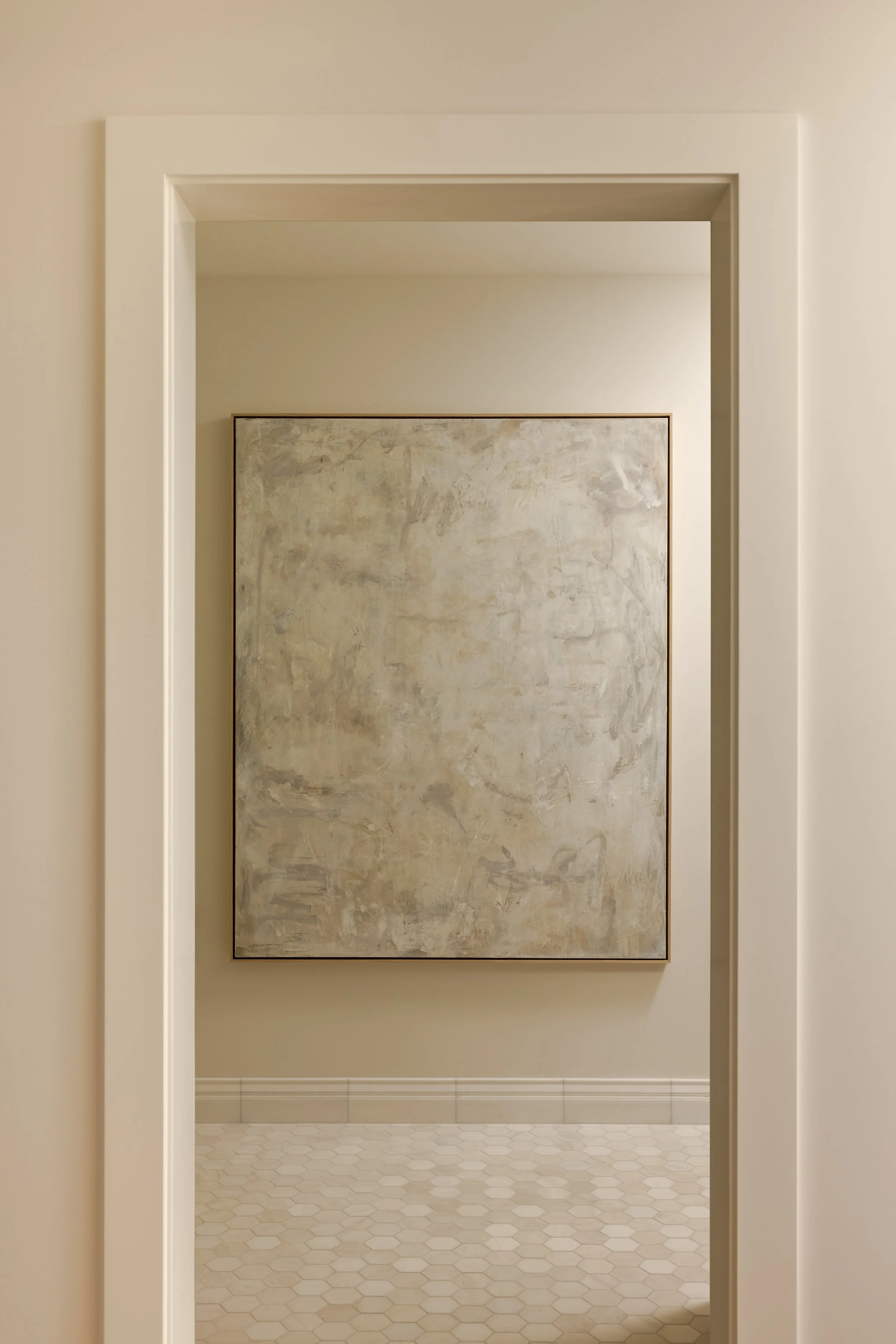 Empty beige room with large abstract painting on the wall and white hexagonal tile flooring.