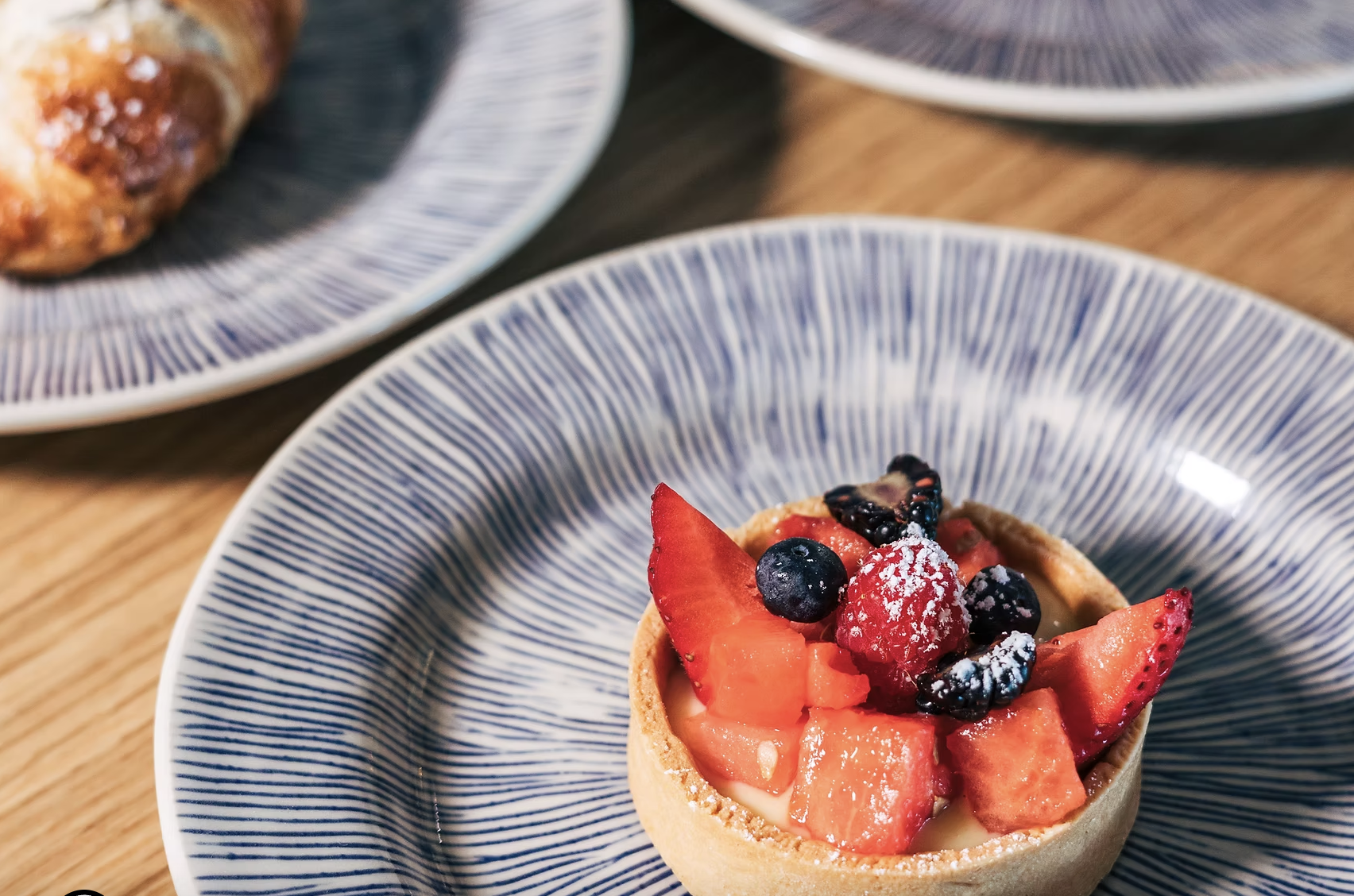 A fruit tart topped with strawberries, blueberries, raspberries, and blackberries on a blue and white striped plate.
