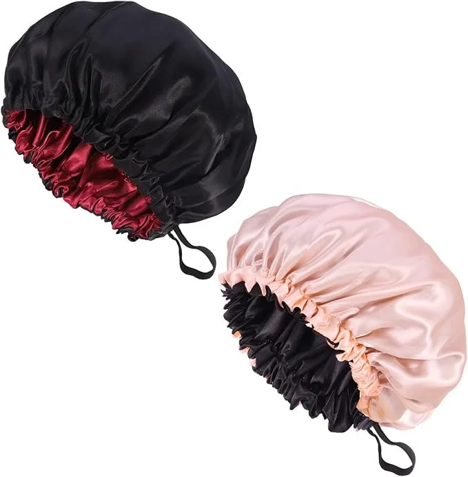 Two satin shower caps, one pink and one black with red interior, set against a white background.