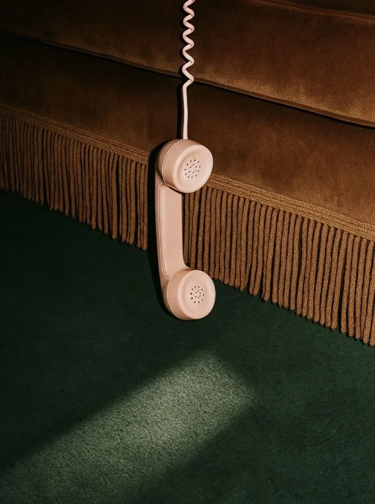 A beige vintage-style telephone hanging from a brown upholstered headboard, casting a shadow on a green carpet.