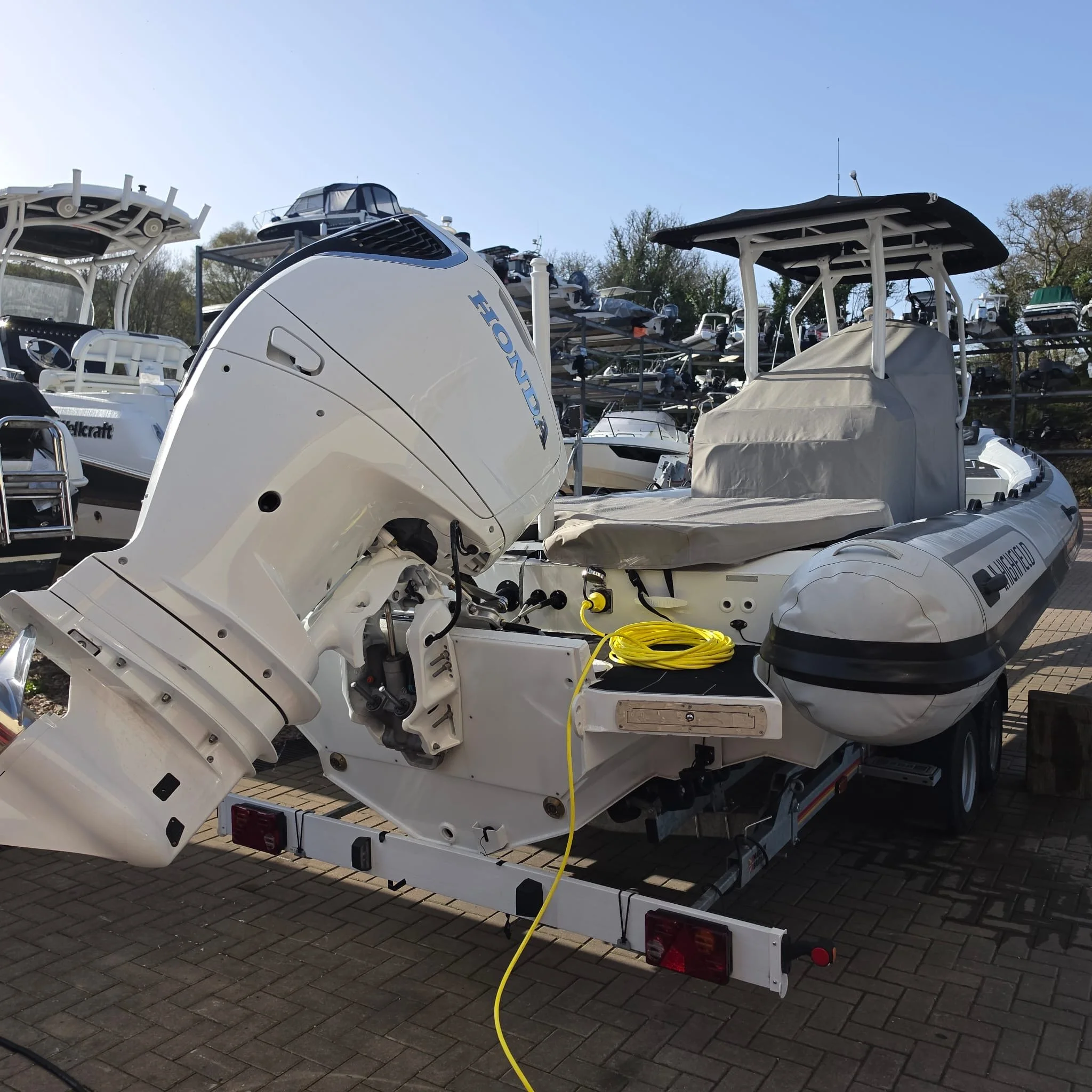 A boat with a large outboard motor on a trailer at a marina with other boats stacked on racks in the background.