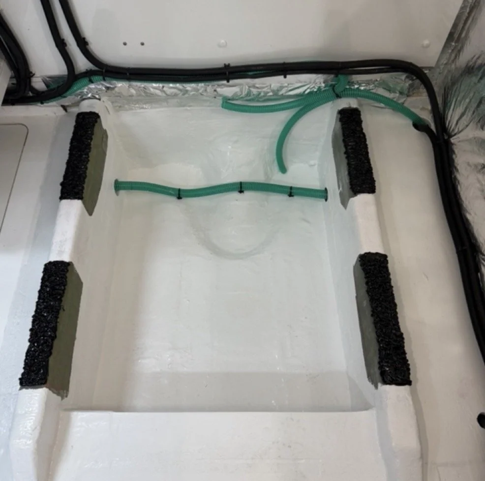 The photo shows an empty white plastic container or tank with black foam padding on its sides and green flexible hoses attached.