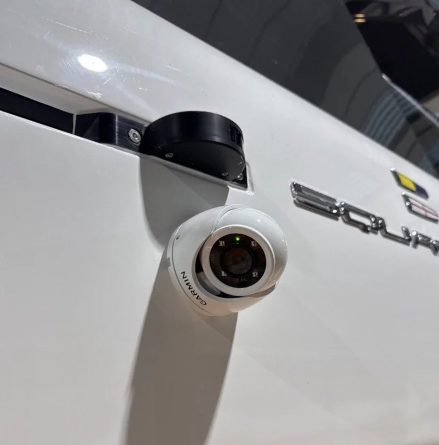 Close-up of a security or surveillance camera mounted on a white surface, with part of a vehicle visible in the background.