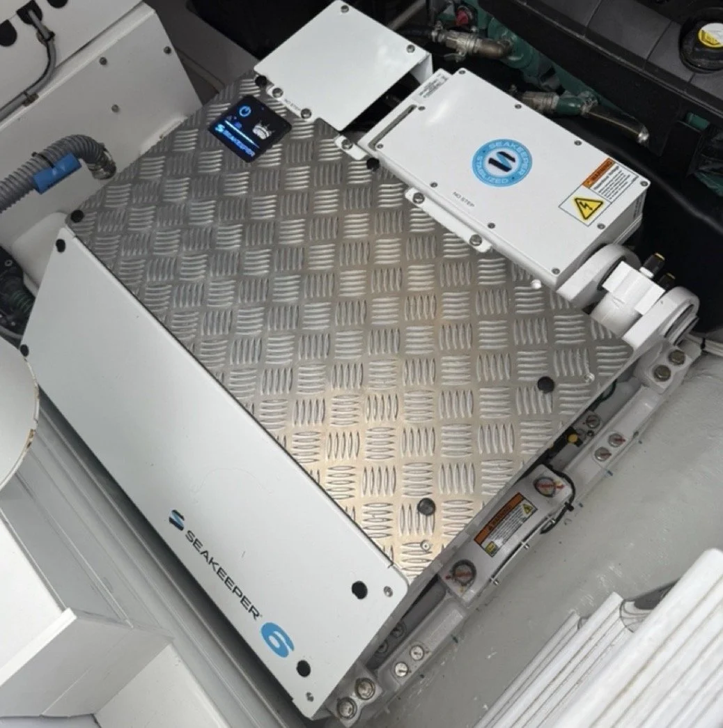 Large white Seakeeper 6 device with a diamond plate metal cover, installed in a marine setting with various cables and components around it.