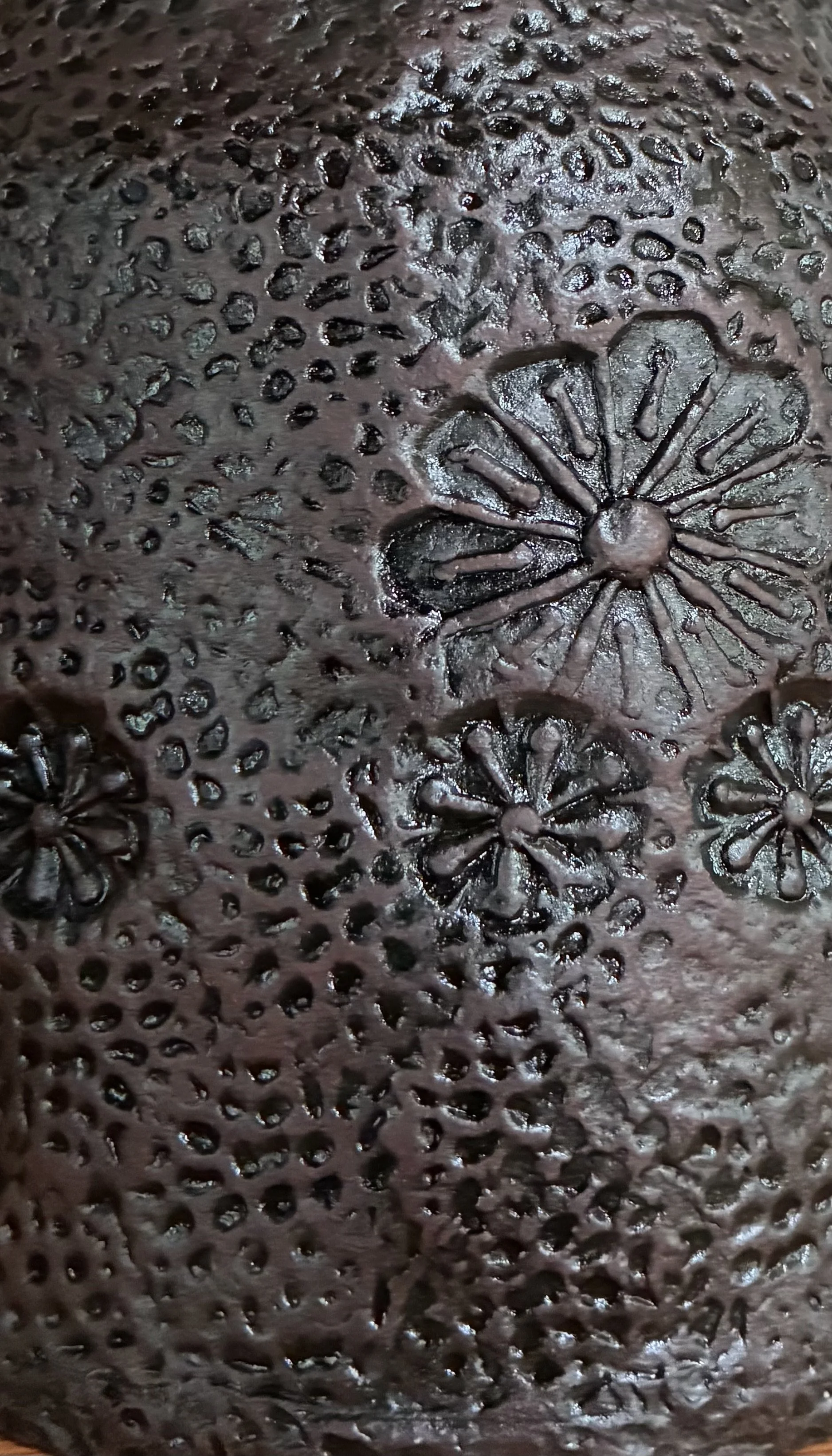 Close-up of a dark, textured surface with small, raised bumps and floral patterns resembling flowers with radial petals.