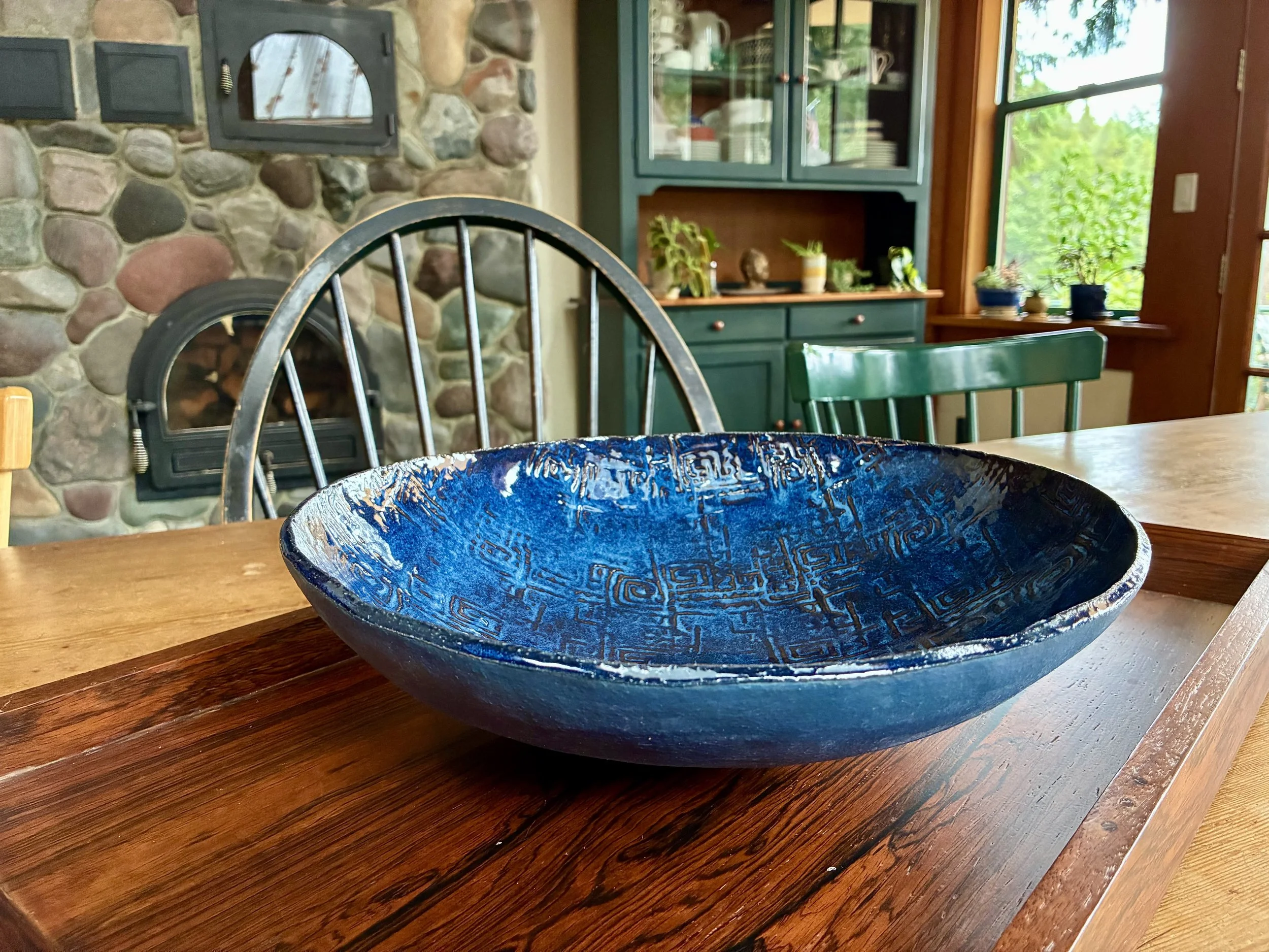 A large, deep blue decorative bowl with intricate patterns on a wooden table in a cozy kitchen or dining area.