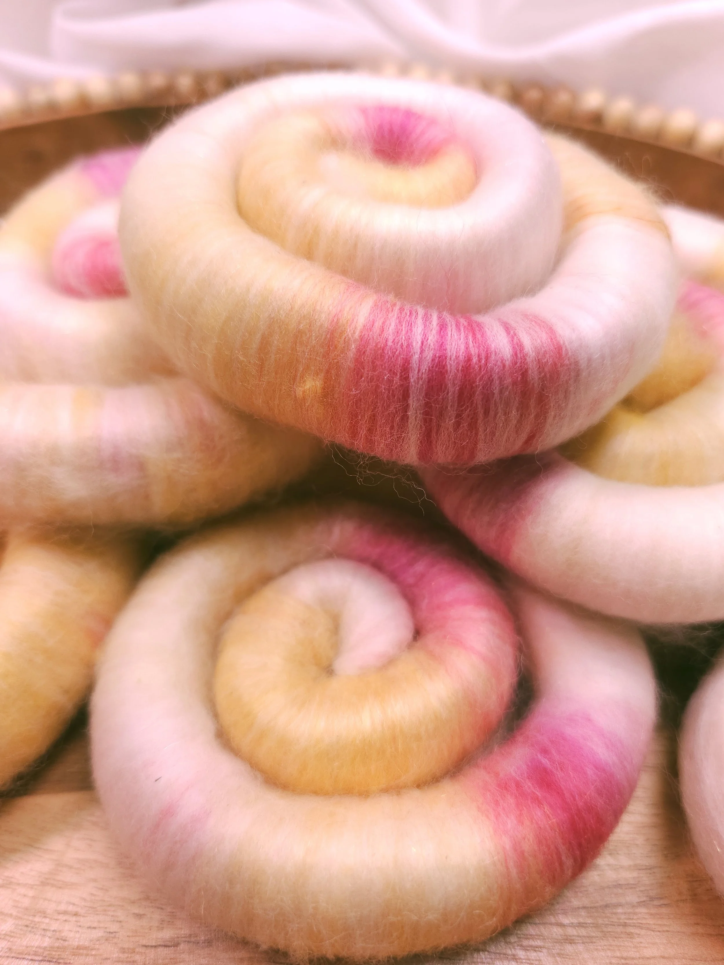 Close-up photo of a pile of colorful pink, yellow and while hand blended wool rolags. Ready for spinning.