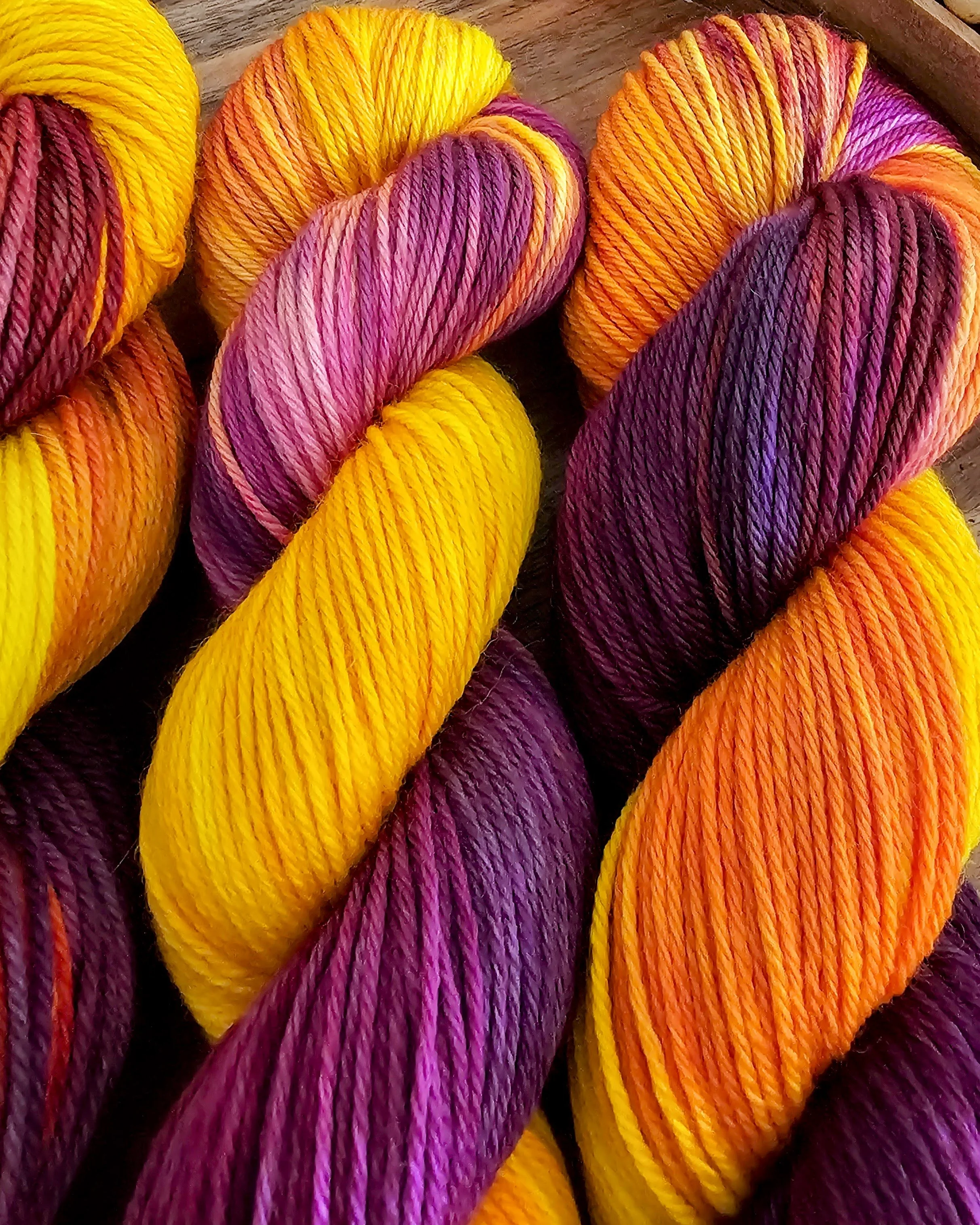 Close-up of colorful hand dyed yarn skeins in yellow, orange, pink, and purple shades.