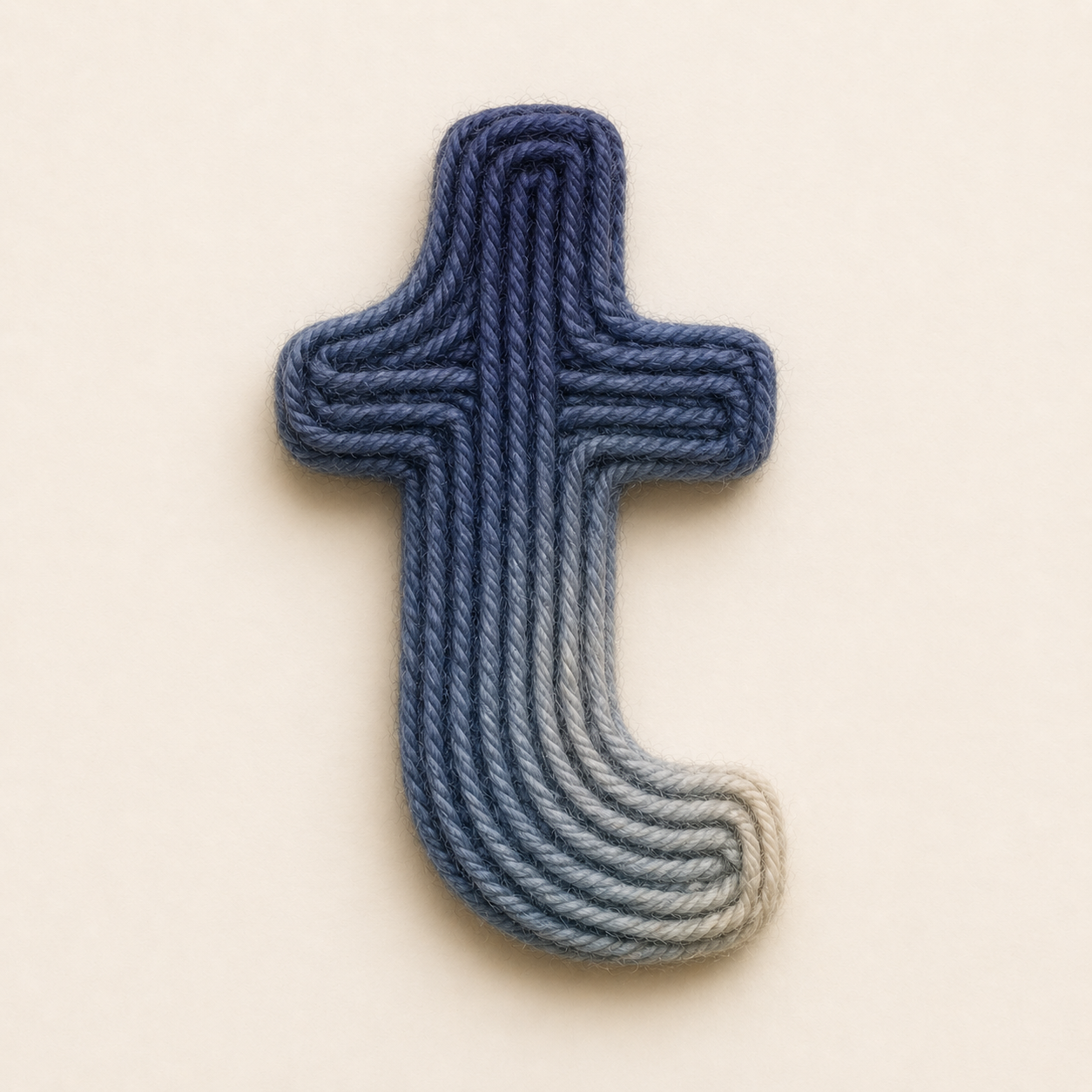 Yarn arranged in the shape of the Tumblr logo, with dark blue on the top and light gray on the bottom, on a plain white background.
