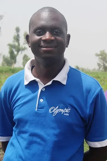 A man outdoors wearing a blue polo shirt with to the word 'Olympic' on it, smiling at the camera.