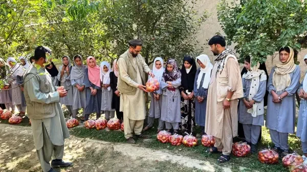 Group of students and teachers standing outdoors under trees, some with hands folded and some with bags of onions placed on the ground in front of them.