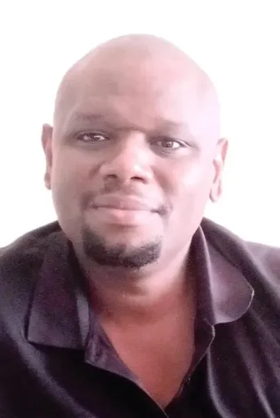 A man with a bald head and goatee wearing a black collared shirt.