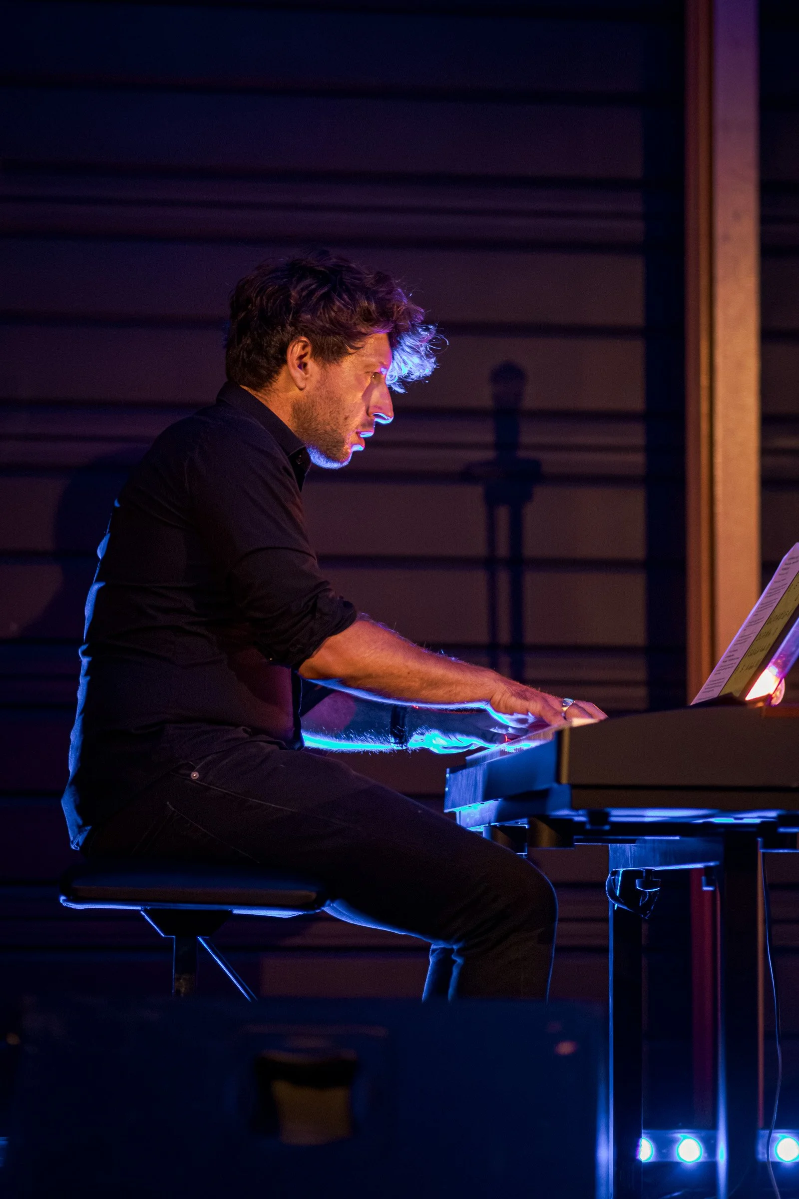 Un homme jouant du piano dans une pièce sombre avec un éclairage bleu et violet.