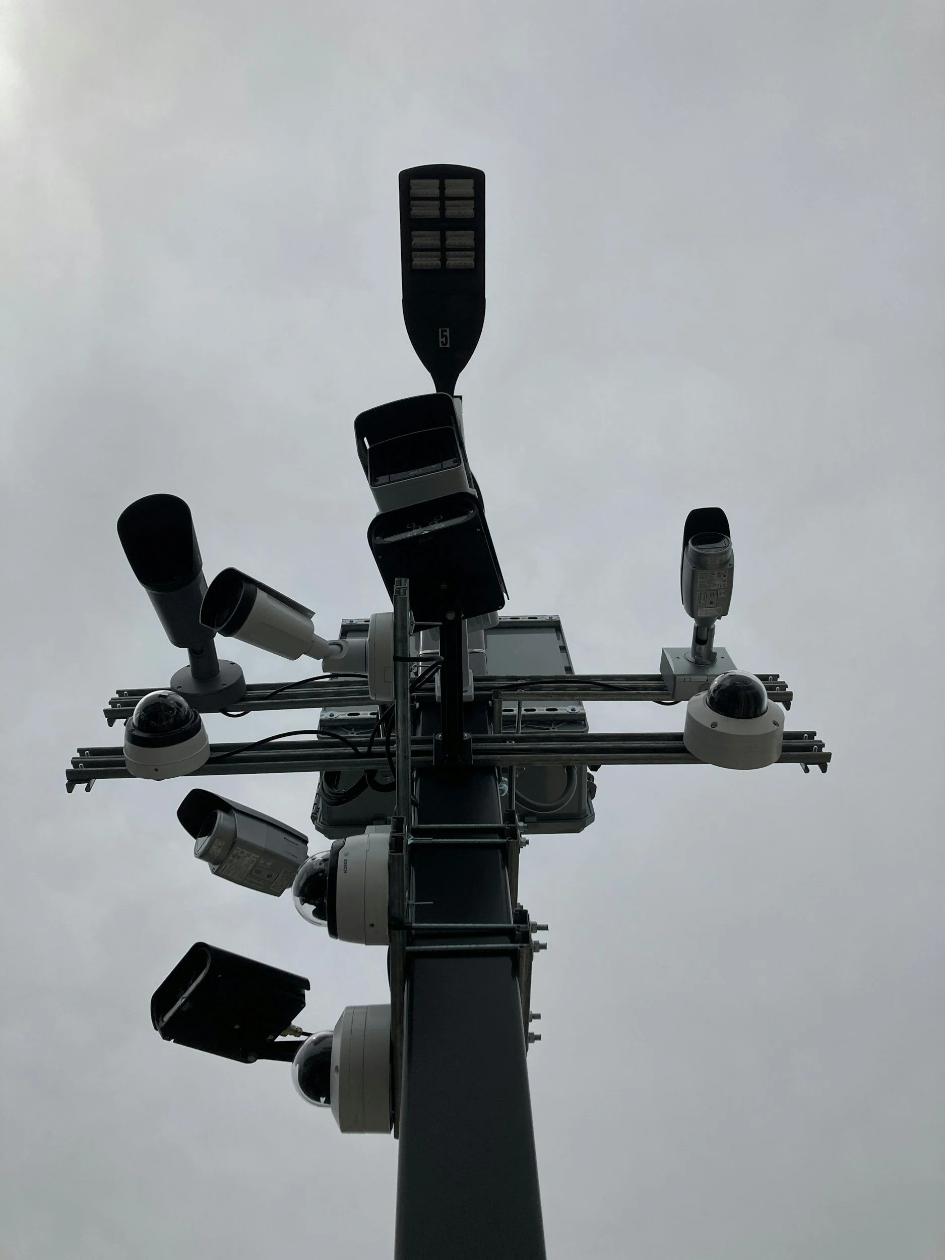 A low-angle view of a communication tower with various antennas and equipment attached, against a cloudy sky.