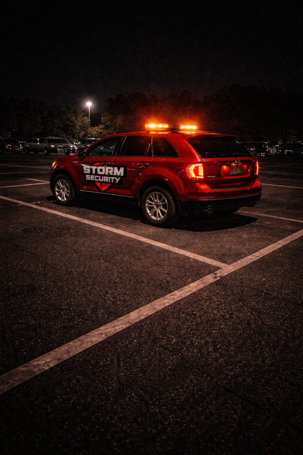 A red Storm Security vehicle with flashing lights parked in a parking lot at night, with other cars and trees in the background.