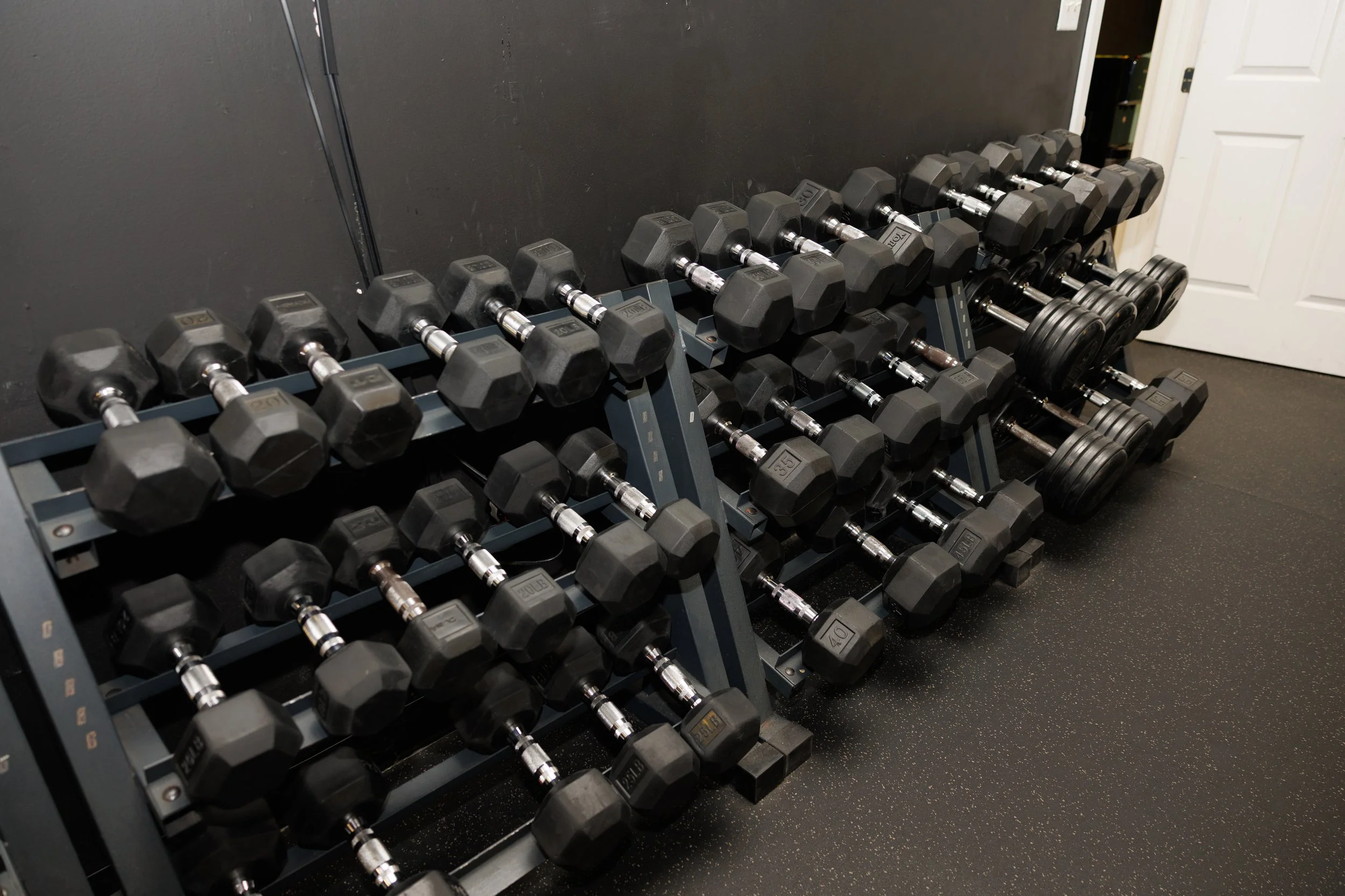 Rack of black adjustable dumbbells on a gym floor.