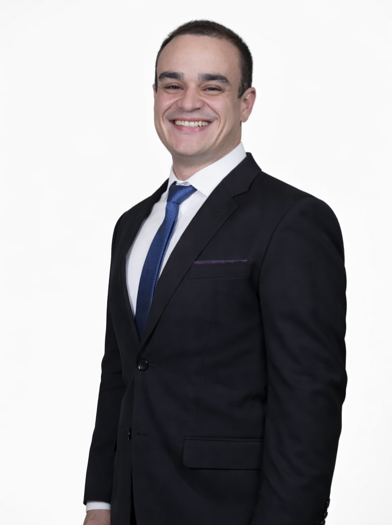 Homem sorridente usando terno preto, camisa branca e gravata azul, posando contra fundo branco.