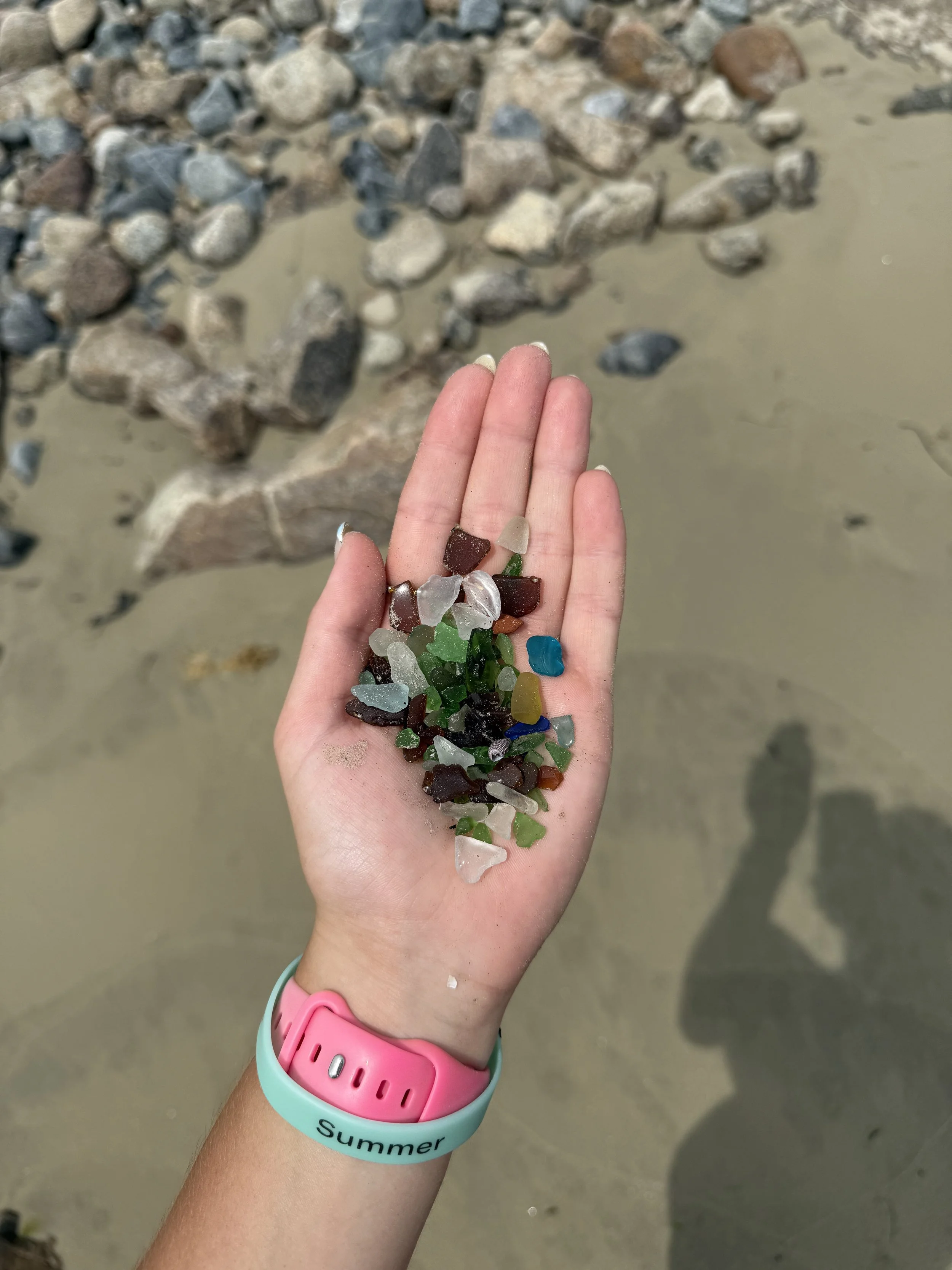 A hand holding a large amount of colored seaglass