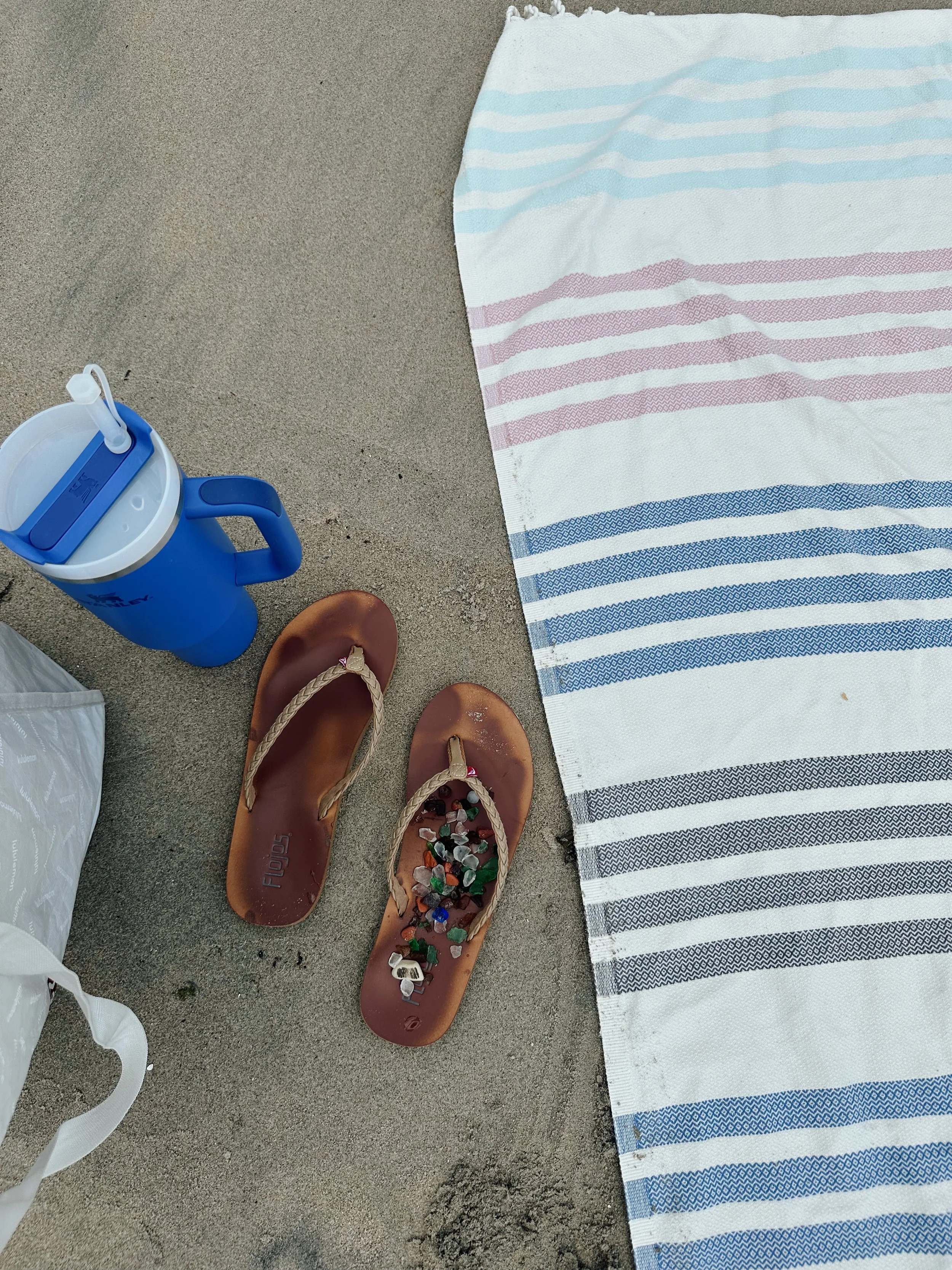 Seaglass on flip flops next to a towel and water bottle