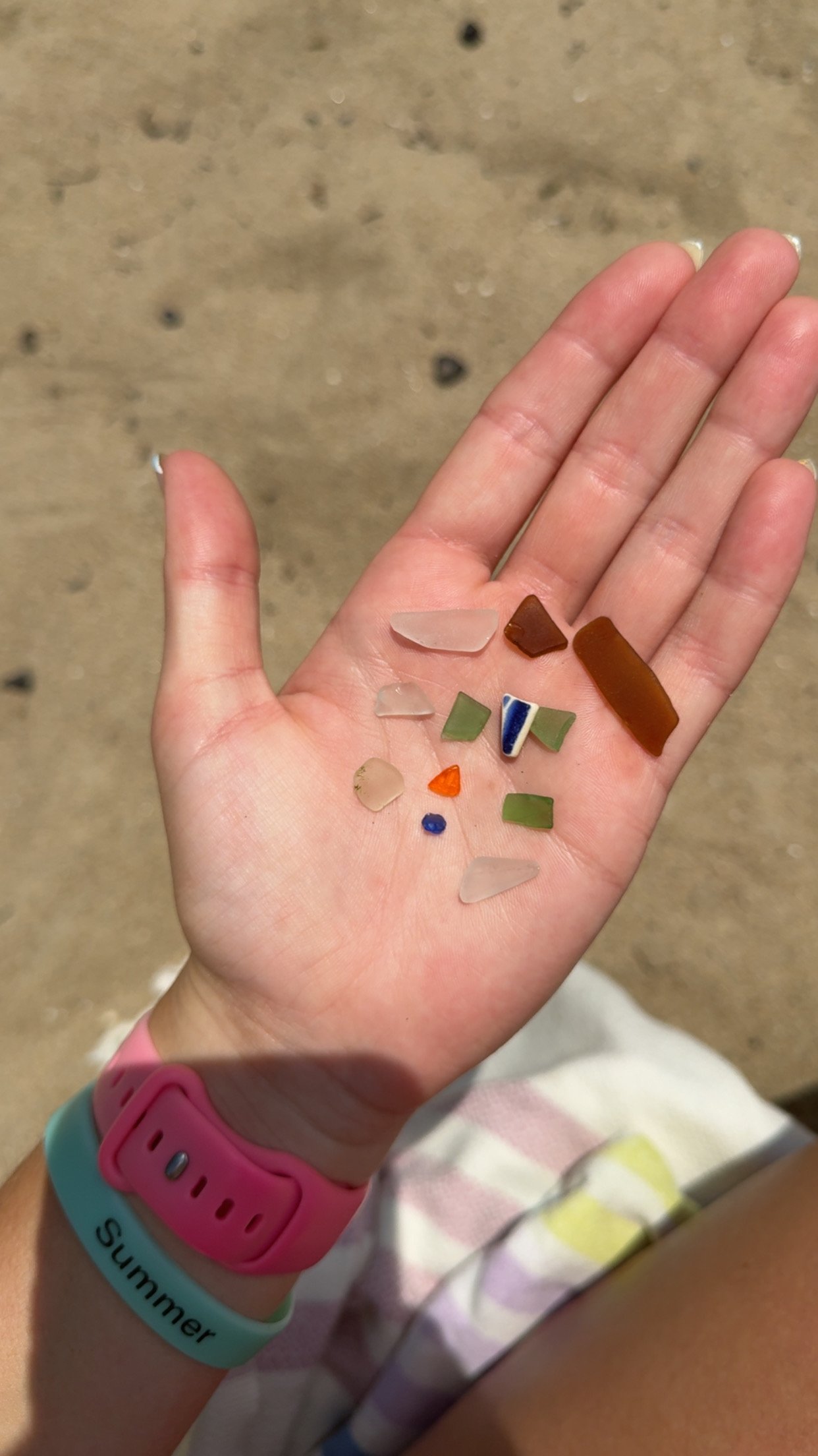 A hand holding seaglass with orange seaglass in it.