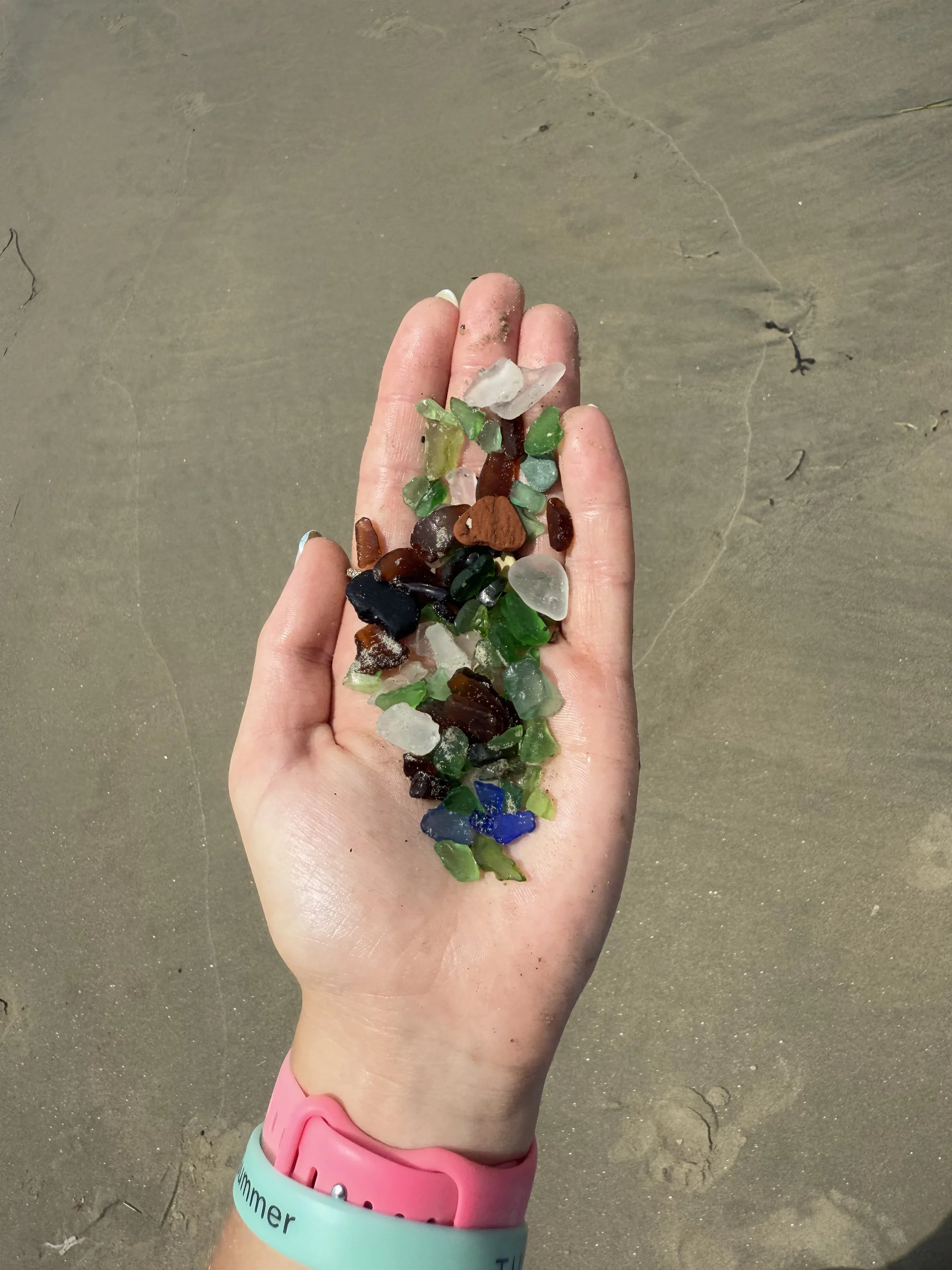 A hand holding special blue seaglass with other colors.
